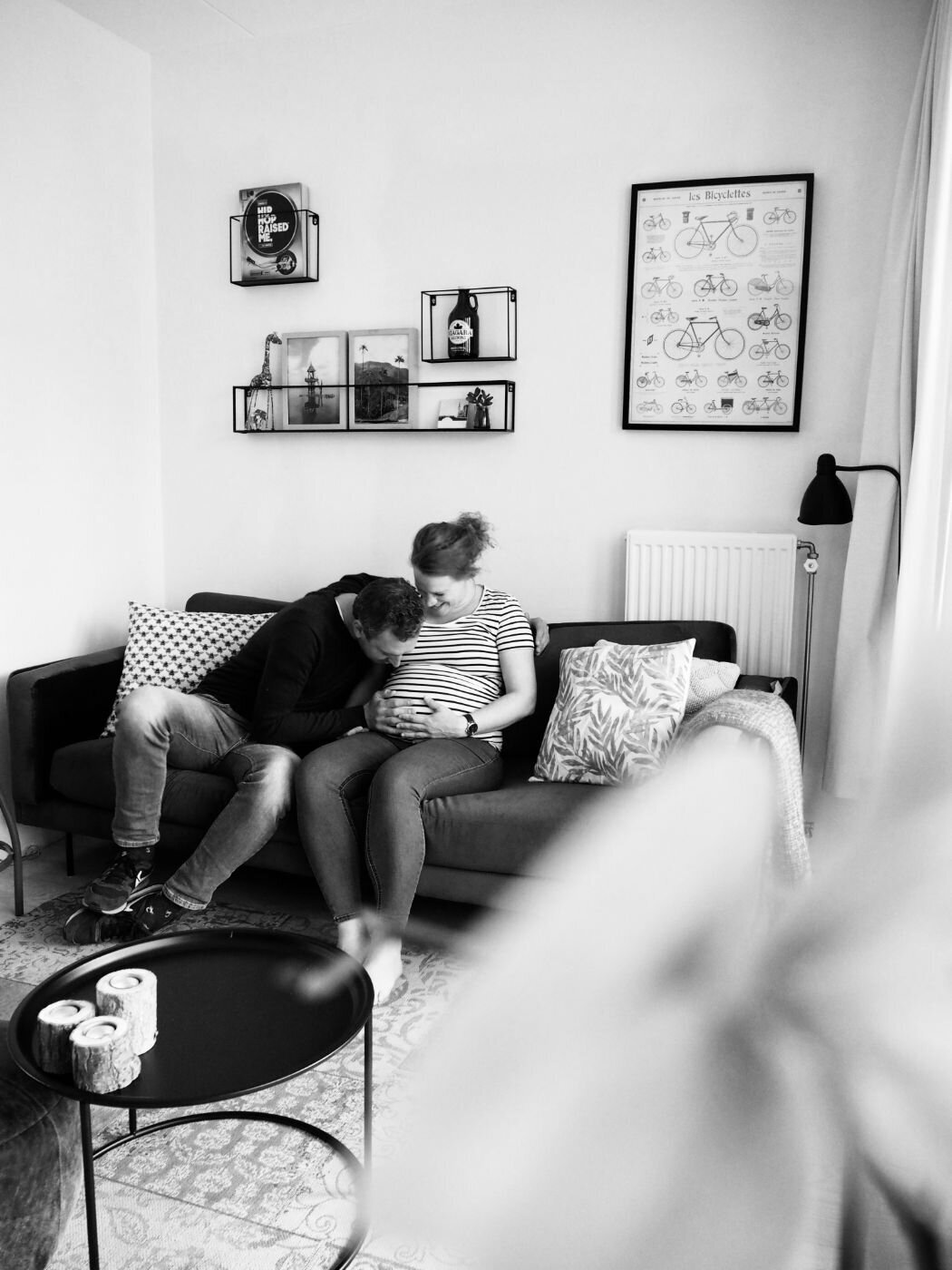Black and white intimate photo of couple on their living room couch, father kissing mother’s pregnant belly