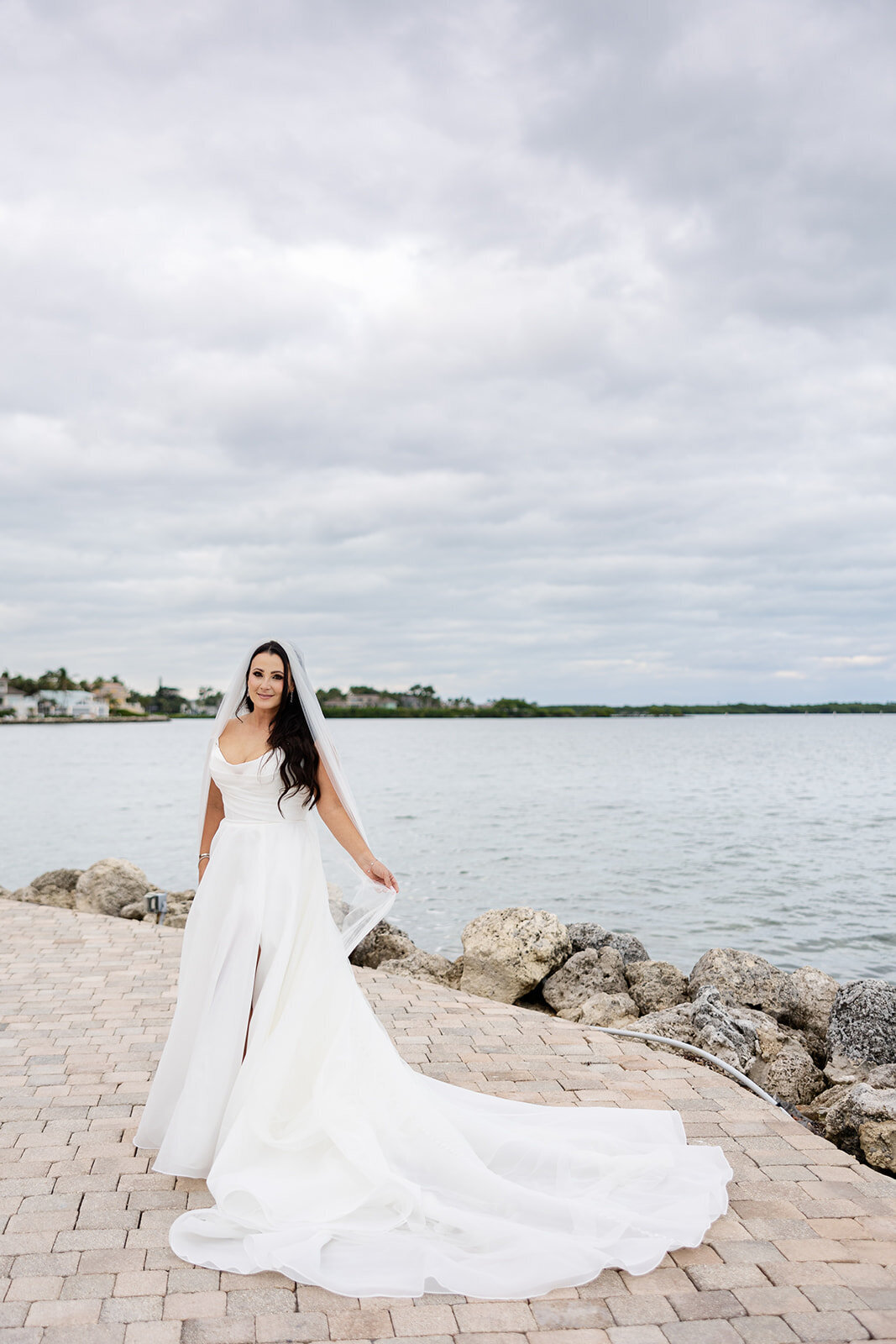 The bride poses gracefully by the waterfront, her flowing gown and serene smile radiating elegance at Ocean Reef, Key Largo.