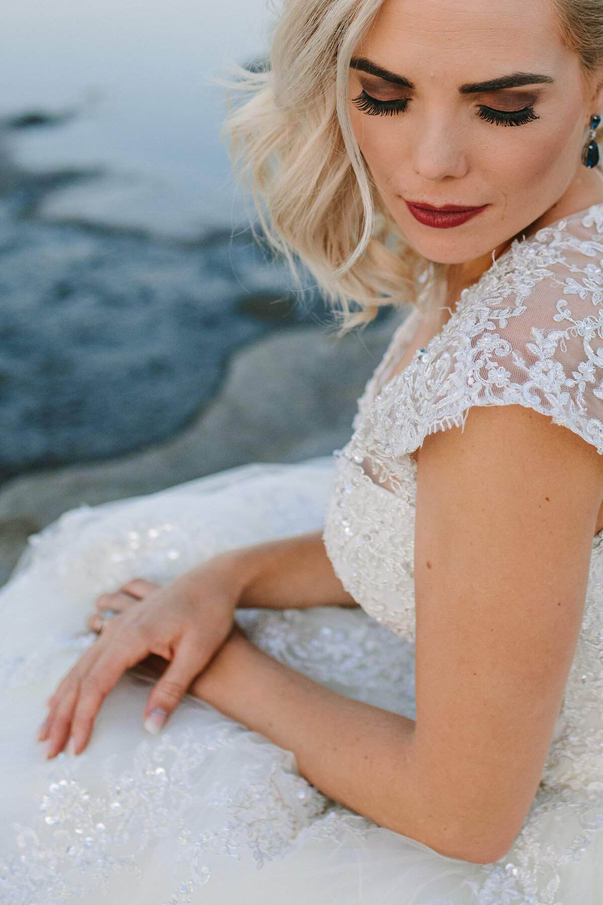 Detailed portrait of bride showcasing her curly blonde hair, vibrant red lips, and graceful hands.