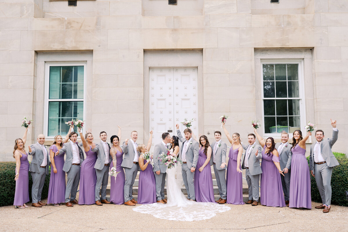 An elegant, joyful wedding party photo taken on the steps of the Capitol building in downtown Raleigh, North Carolina, capturing sophisticated city vibes and celebratory energy by North Carolina wedding photographer Jessica Leigh Mason.