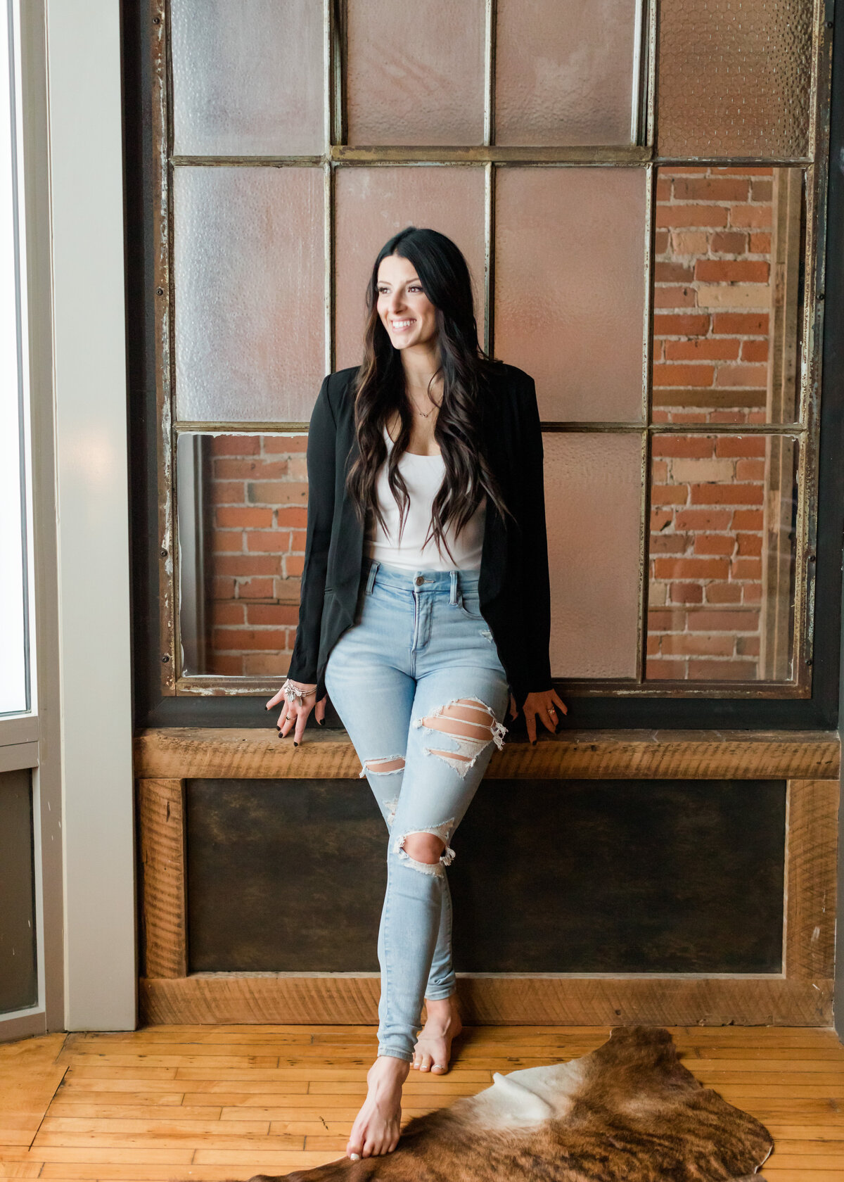 Portrait of Allie Clark, founder of Allie Clark Designs, smiling and standing confidently in front of a brick and glass wall.