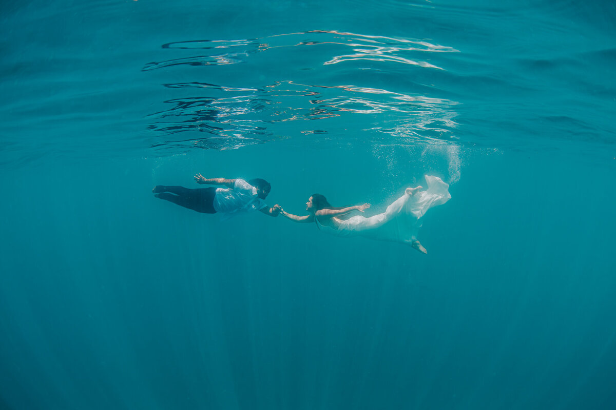 Couple underwater in wedding clothes holding hands