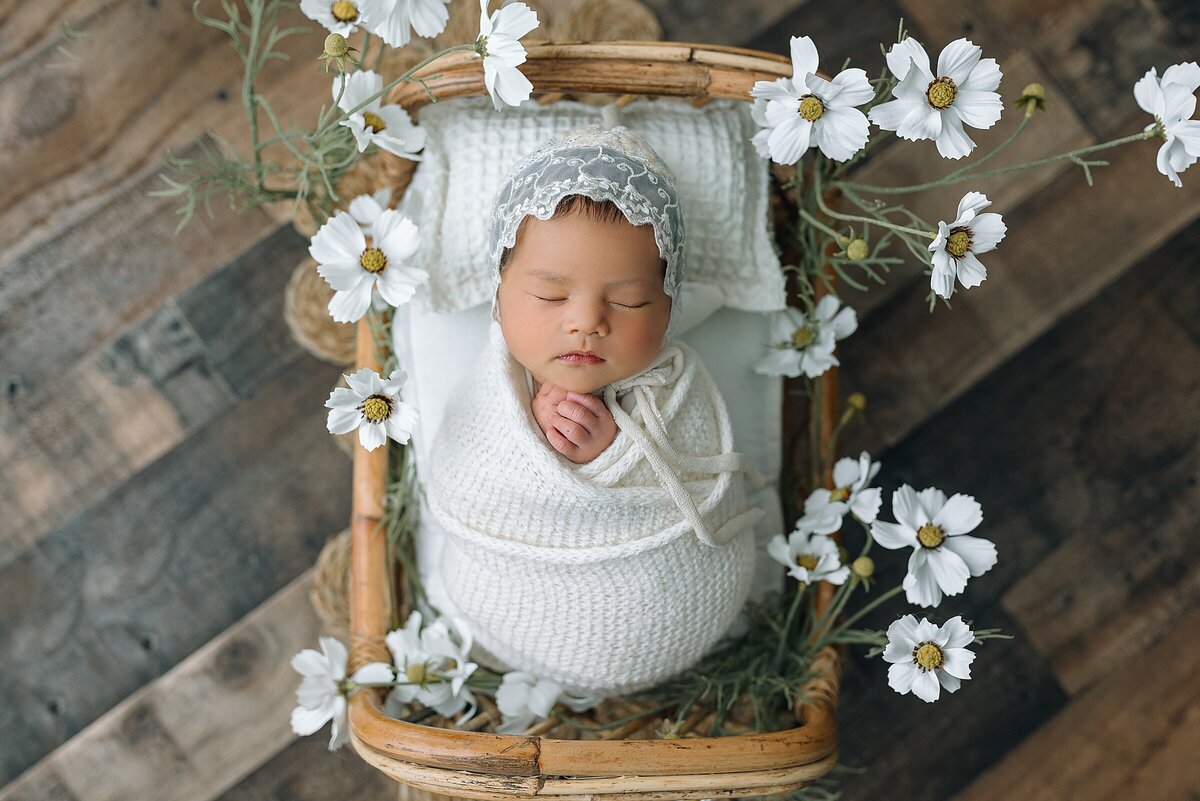 Newborn girl in tiny wooden bed with flowers