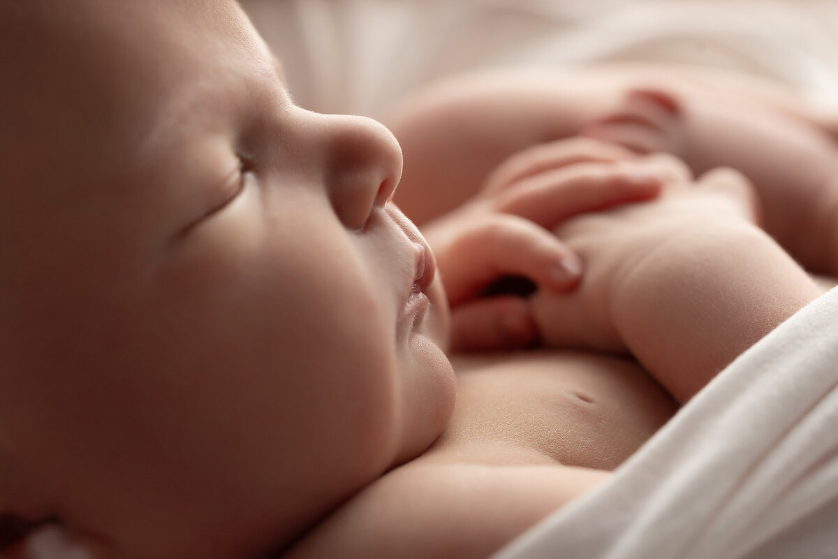 Close-up photo of a sleeping baby’s peaceful face and hands resting on their chest, captured in soft natural light by a Dallas Newborn Photographer specializing in baby photography.