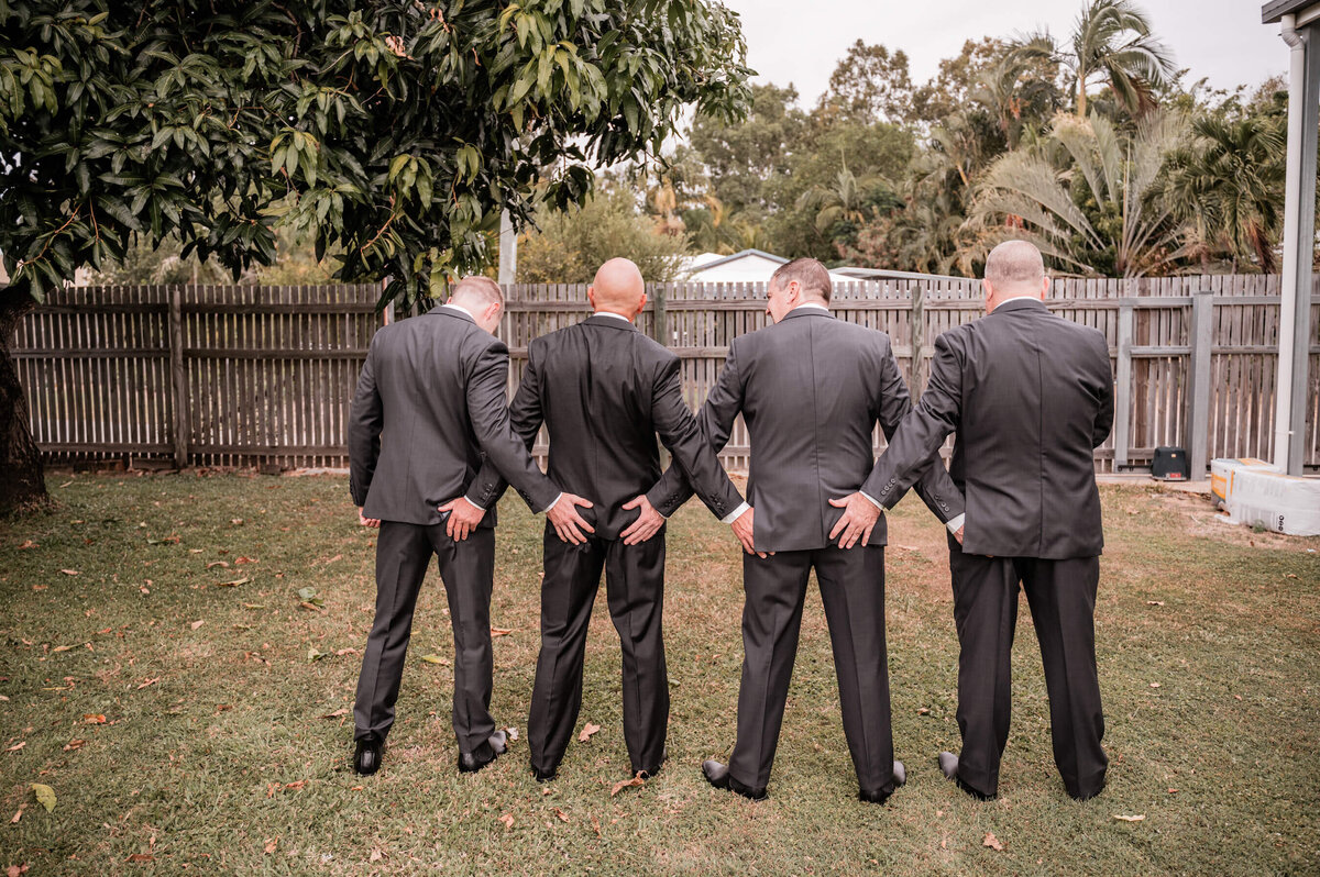 A cheerful group of groomsmen in formal suits standing in a picturesque yard, ready for the wedding festivities. - photo by Jamie Simmons