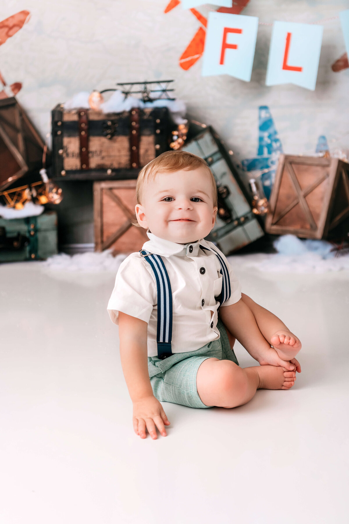 Portrait Photographers CT create timeless first birthday portraits of baby boy in white button-up shirt with navy suspenders and vintage aviation backdrop