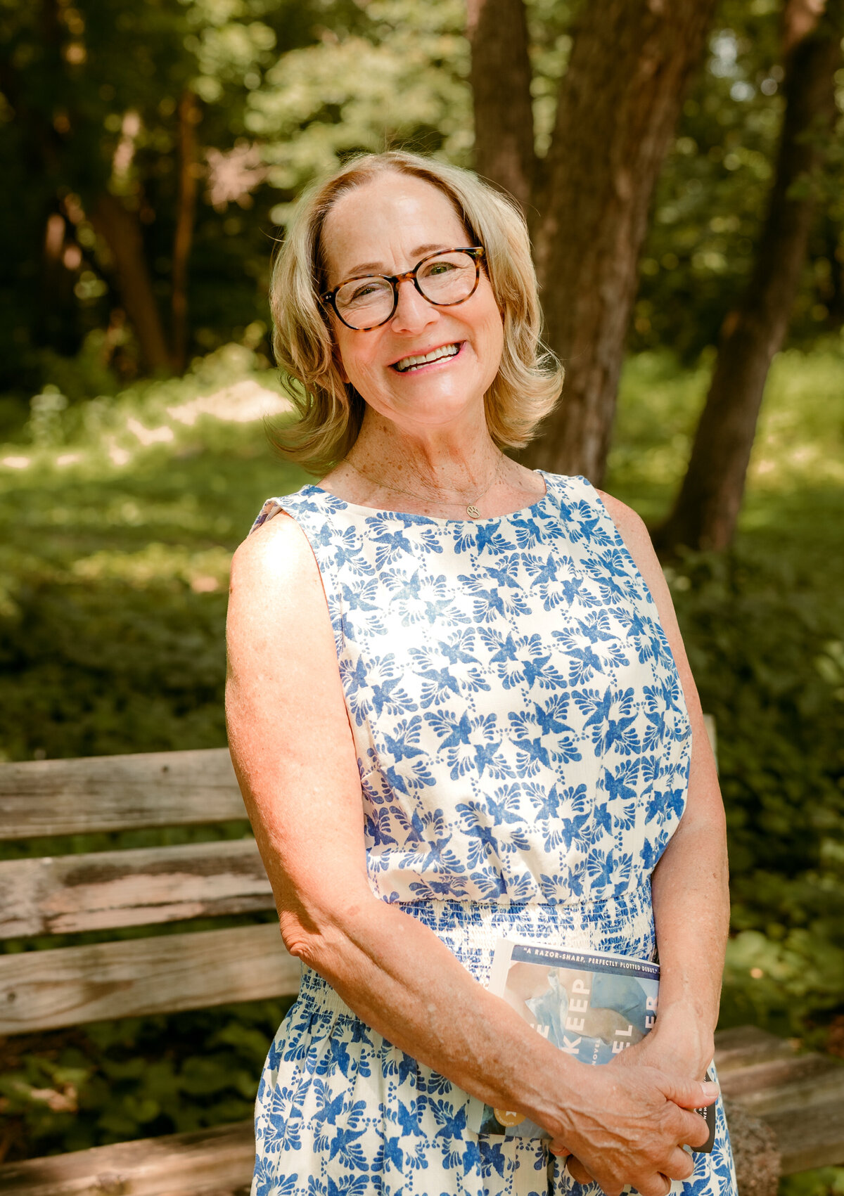 Professional online dating profile photo of Linda sitting on a park bench in the Twin Cities, wearing glasses and a blue floral dress.