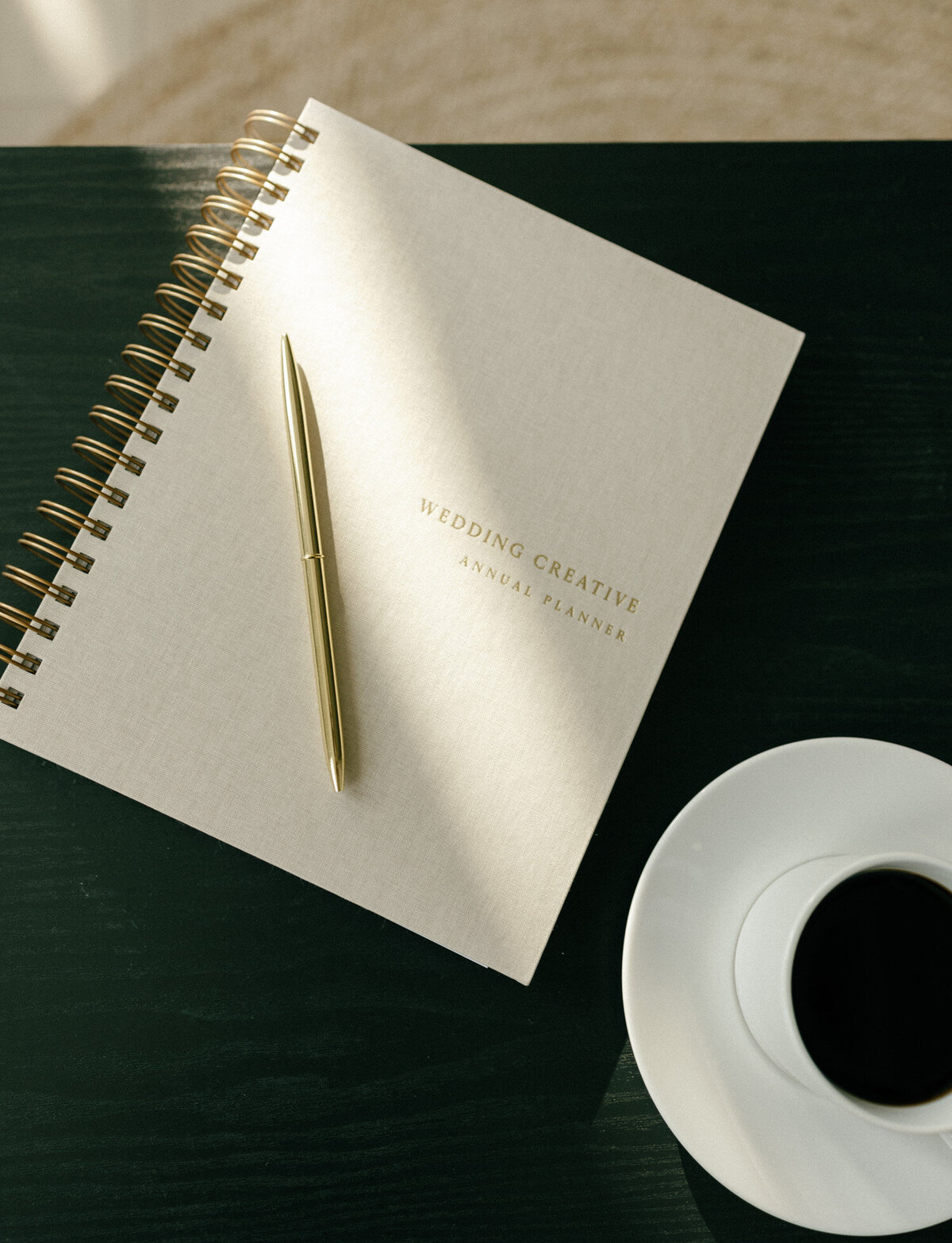 beige linen journal with gold pen, gold foil lettering, coffee cup on black coffee table