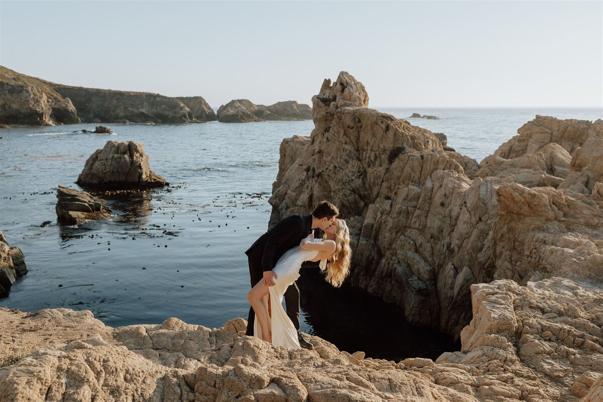 bride and groom standing on rocks in the ocean