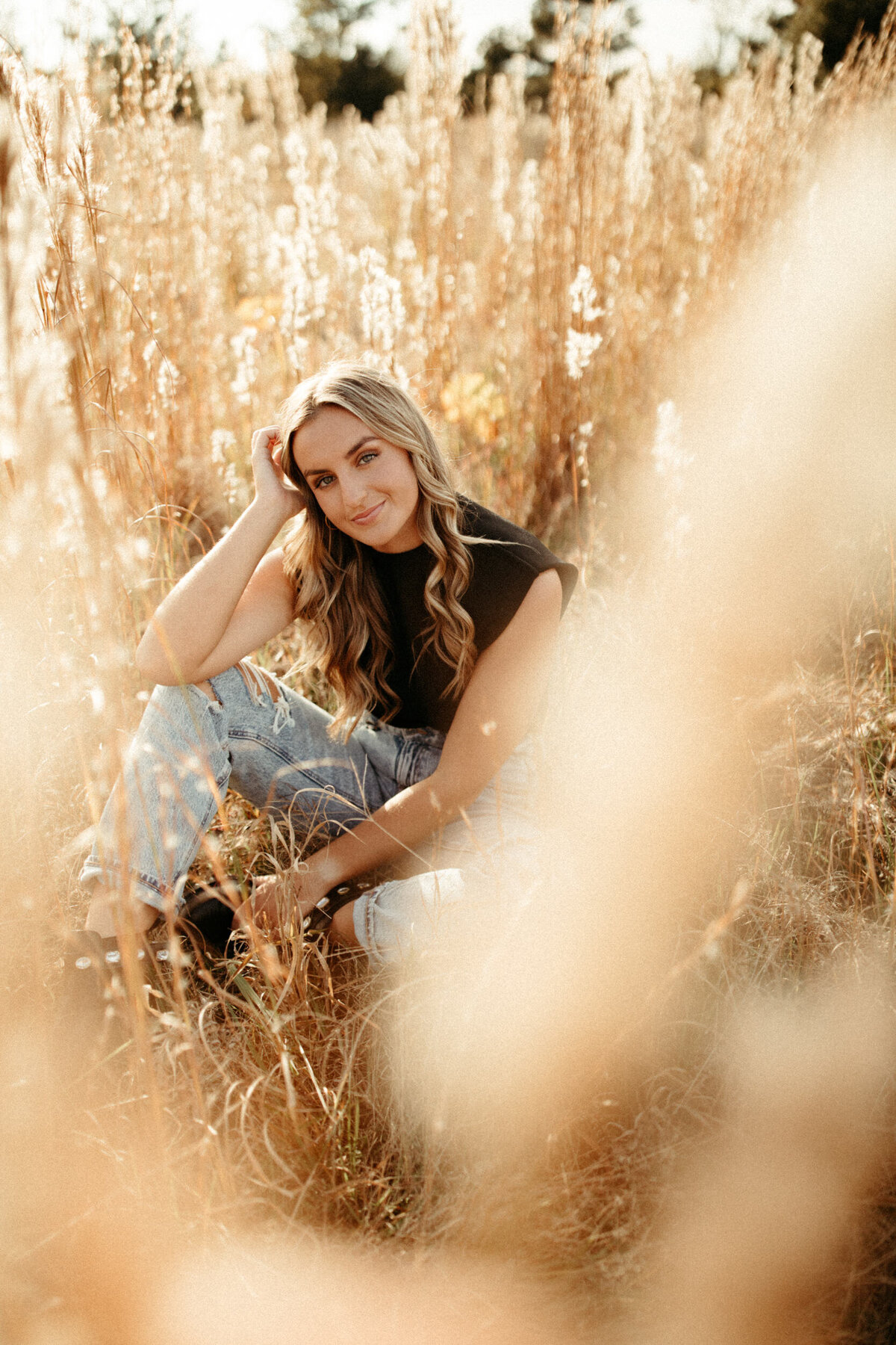High school senior girl sitting in a field with tall grass and pampas grass