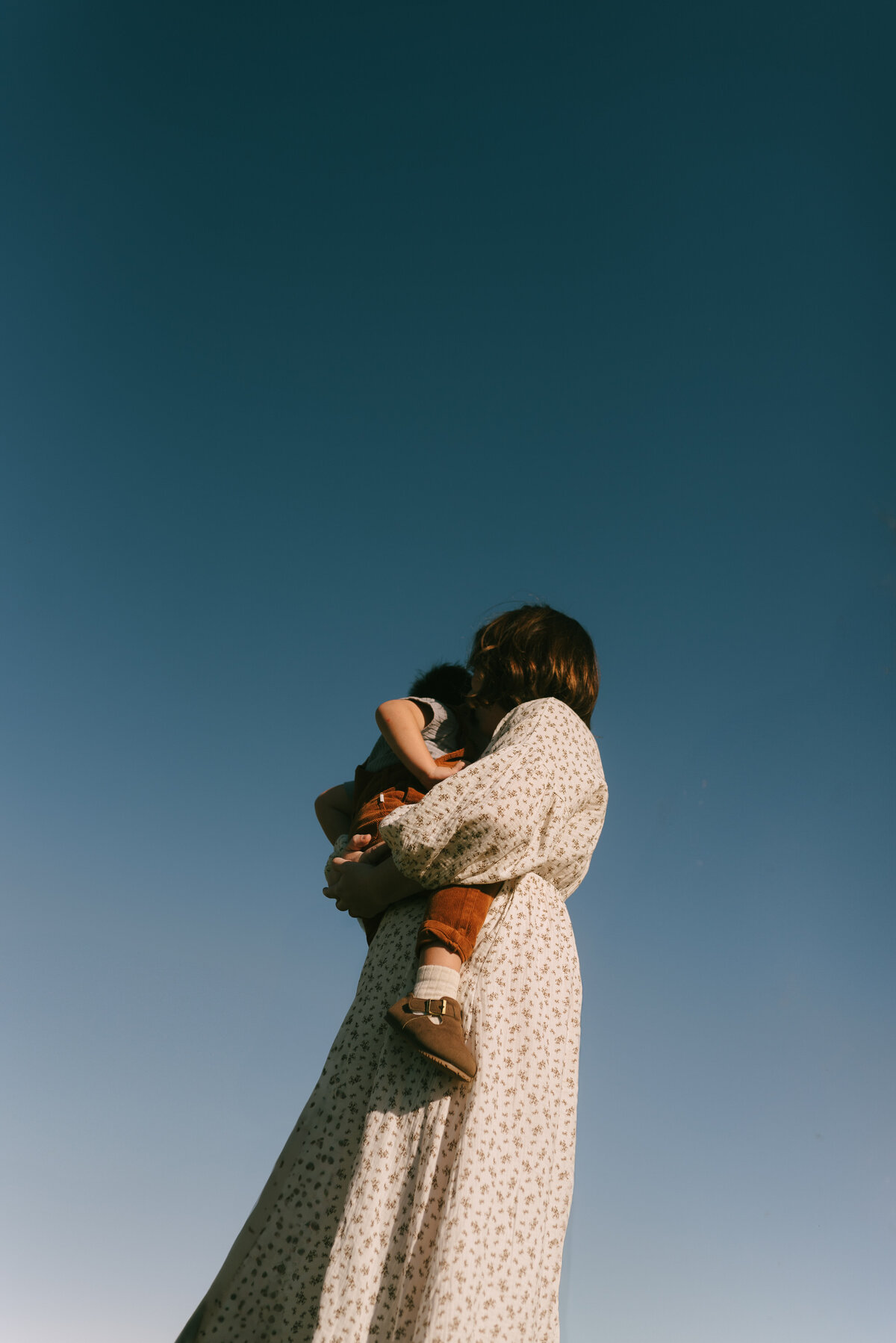 a mother holding her son with the deep blue sky above them.