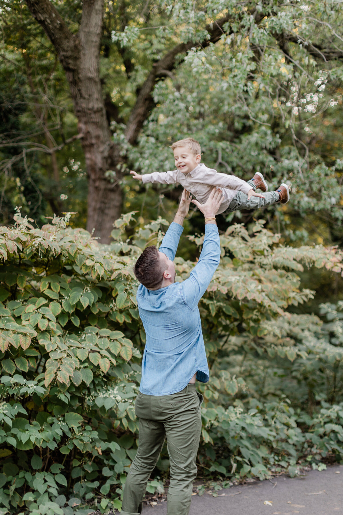 Dad tossing his son in the air in a lush green park photographed by Family Photographer South Jersey Tara Federico