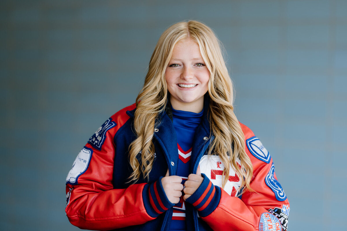 Sabine high school senior cheerleader wearing letterman jacket standing in front of blue wall
