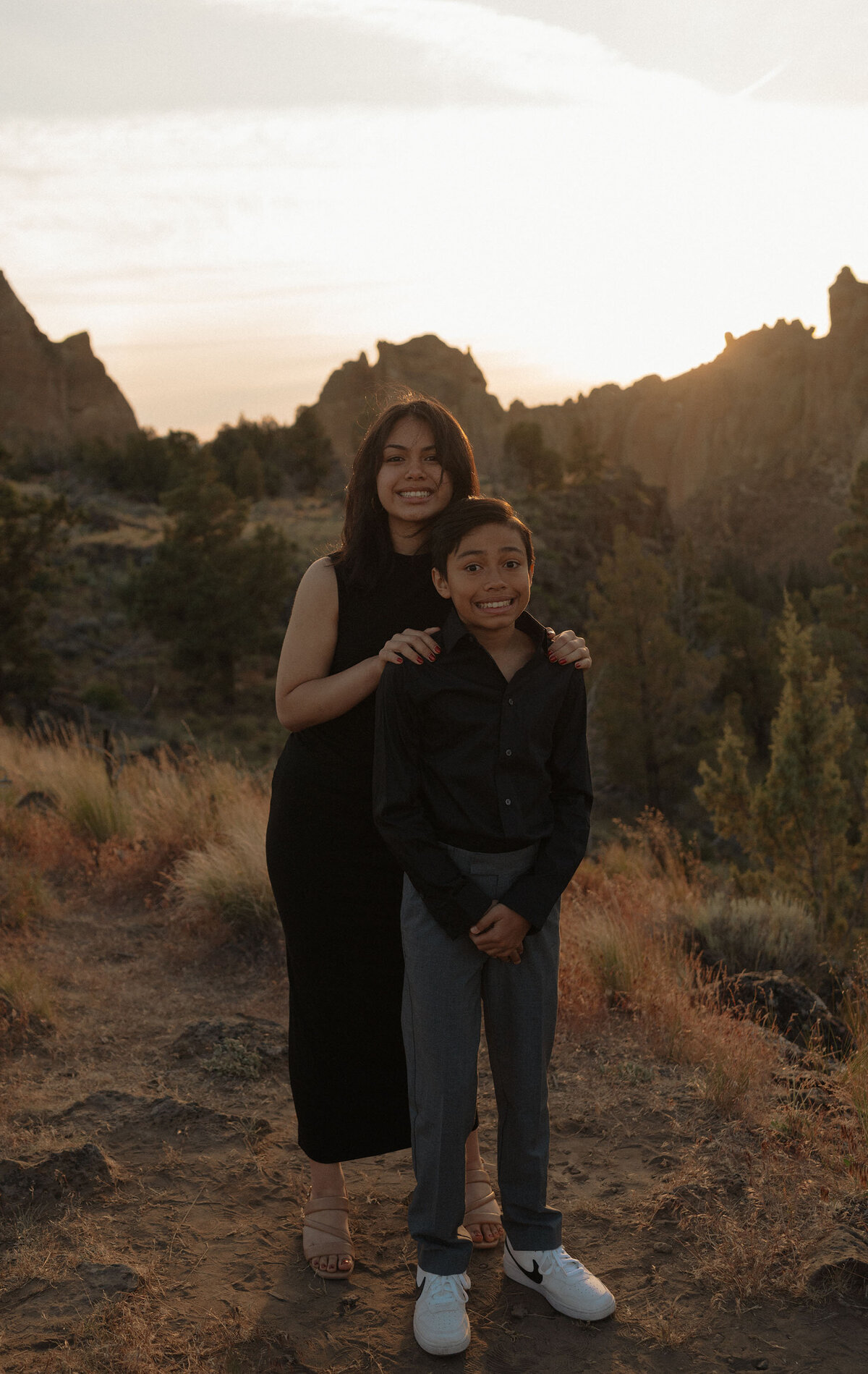 brother and sister wearing black and standing in front of the tall rocks at Smith Rock State Park