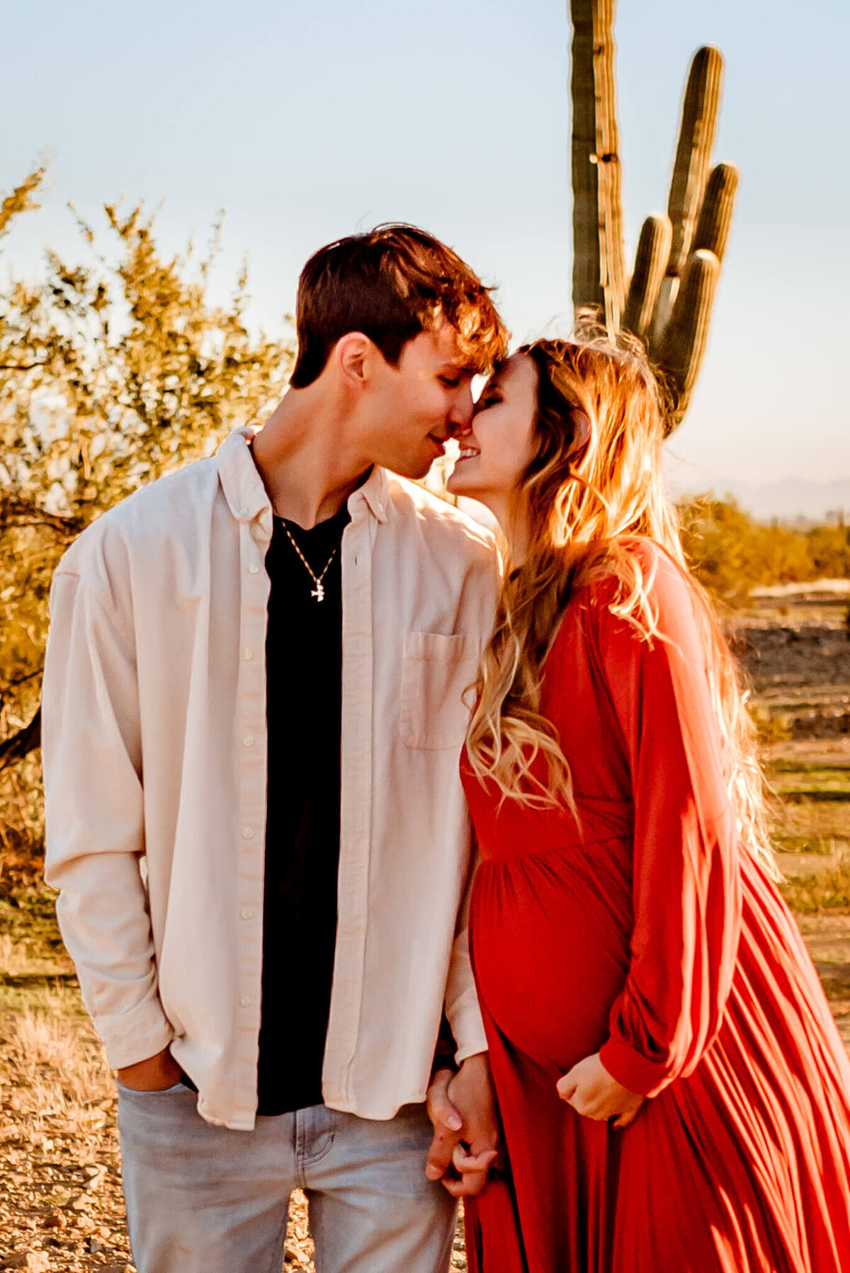 rust maternity dress on mom who is kissing dad for maternity photos in AZ