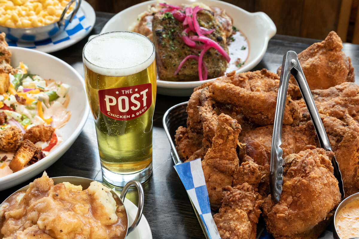 A fresh pint of beer from The Post Chicken and Beer in Denver, Colorado. Pictured with it are plated fried chicken dishes and sides.