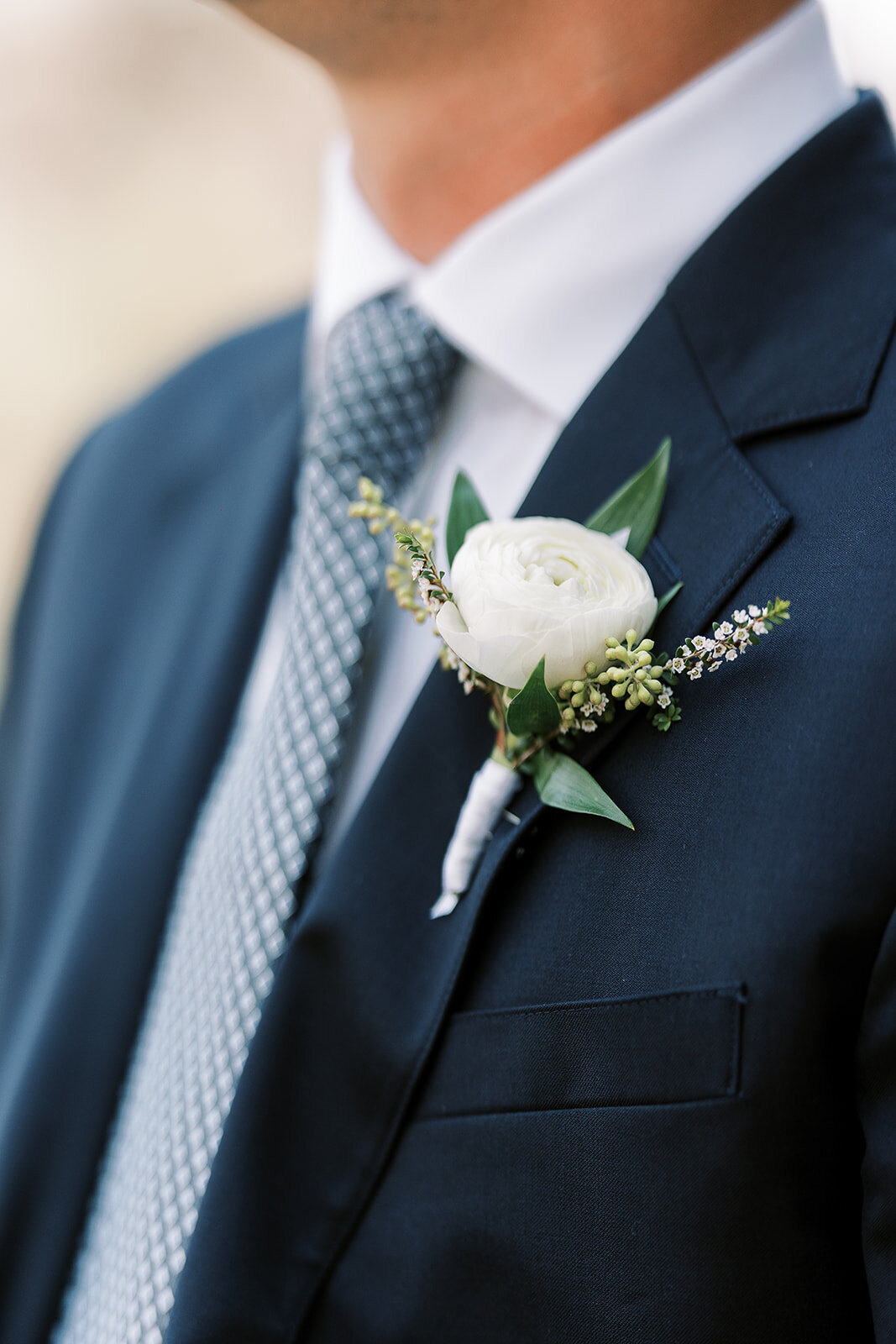 White ranunculus boutonniere with ruscus on blue suit jacket