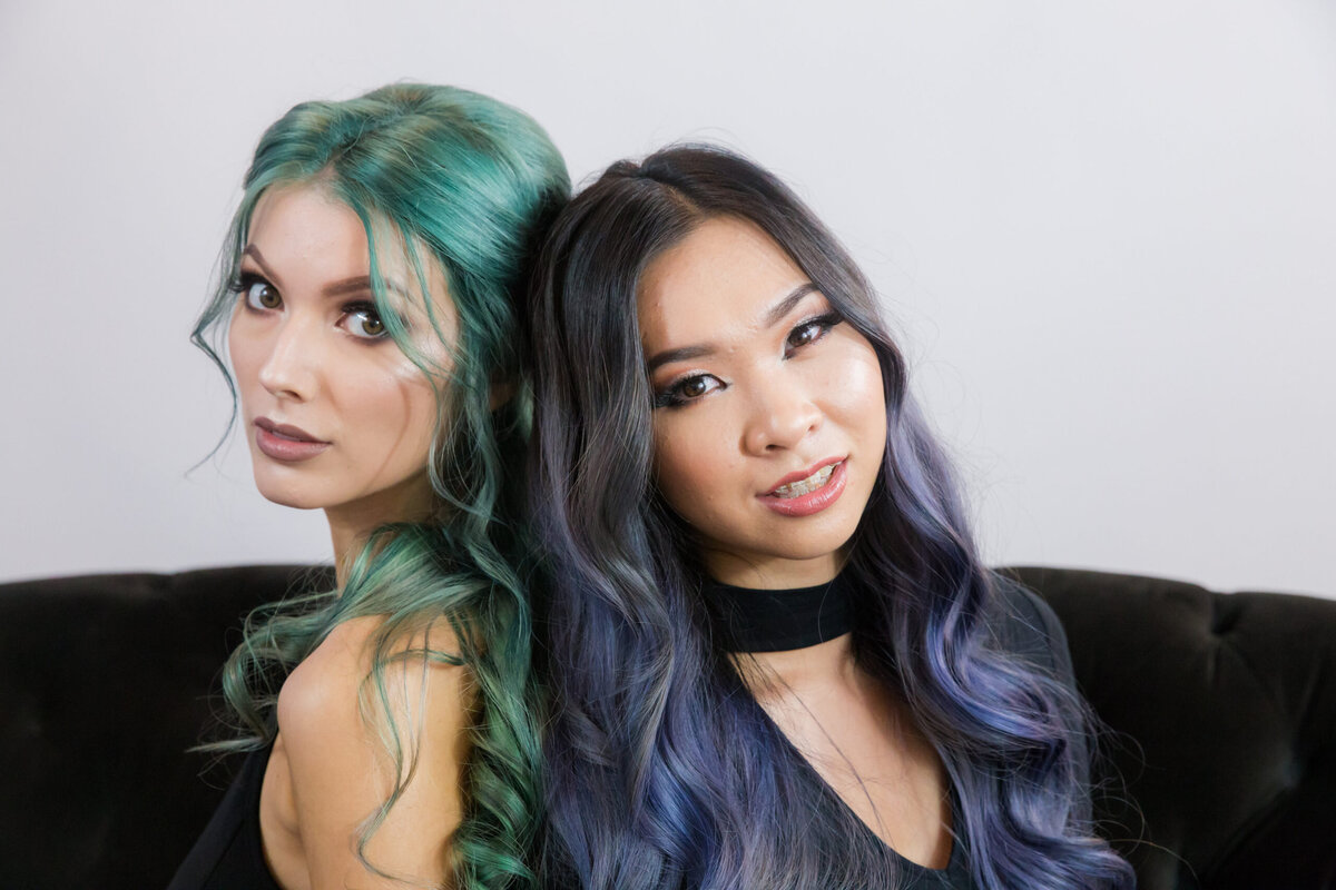 Two models seating together with blue and green metallic hair colour