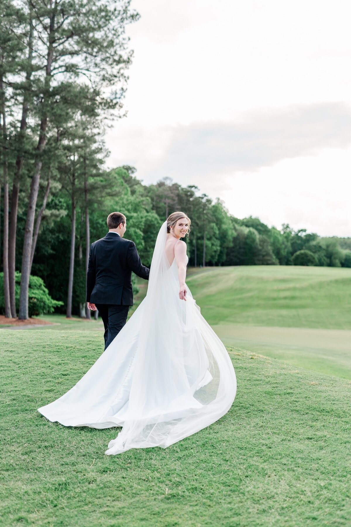 The bride looks back over her shoulder as she and her husband walk across a country club field at a wedding near Greensboro, NC.