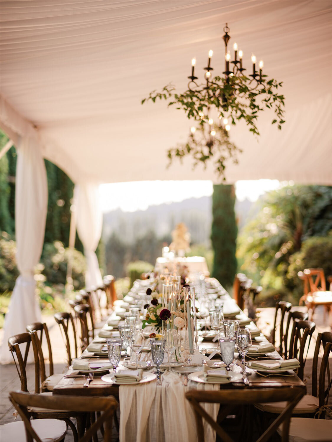 A long dining table set under a white tent with chandeliers