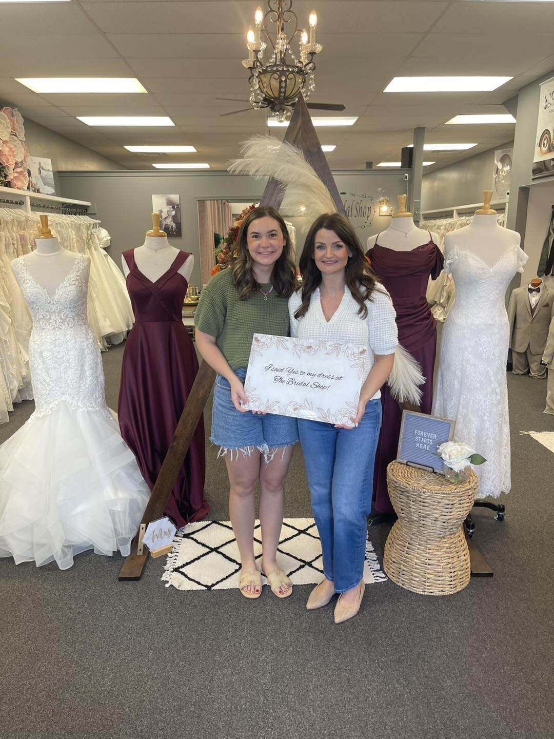 Two women standing together in a bridal shop holding a sign after choosing a dress