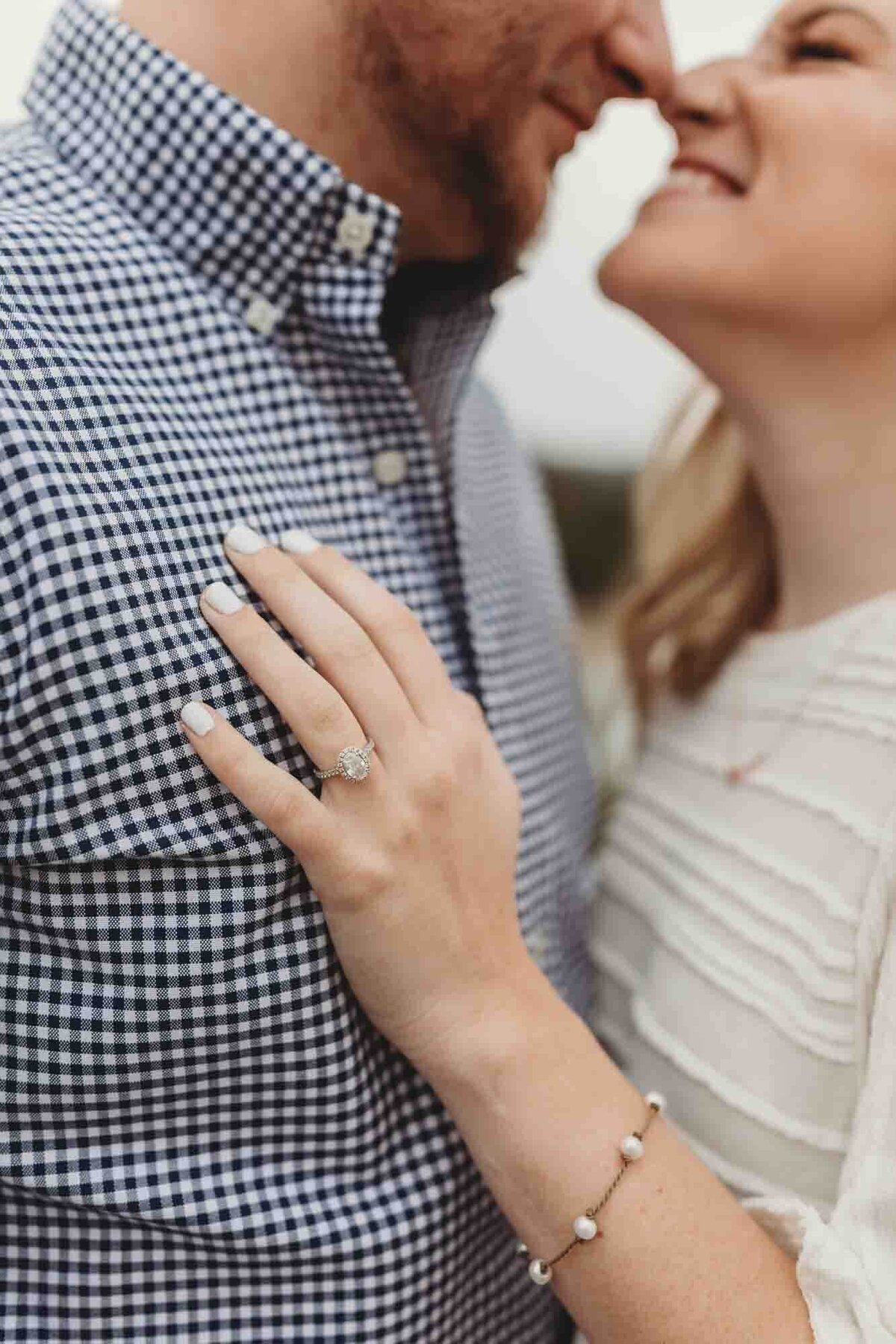 engaged couple snuggle noses with each other, while she shows off her engagement ring on his chest.