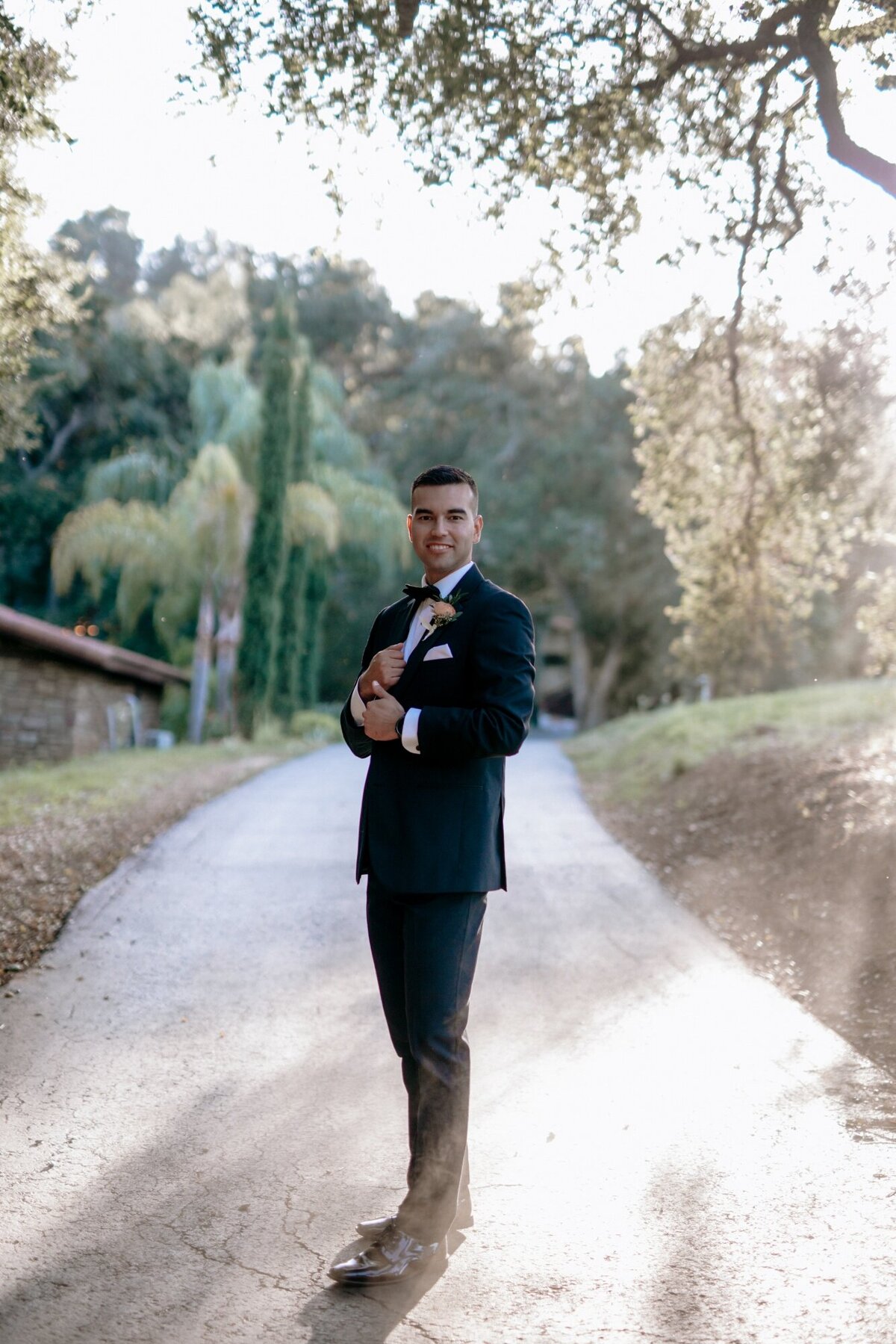 Groom posing on the road at the winery in Temecula with his hand on his cufflinks.