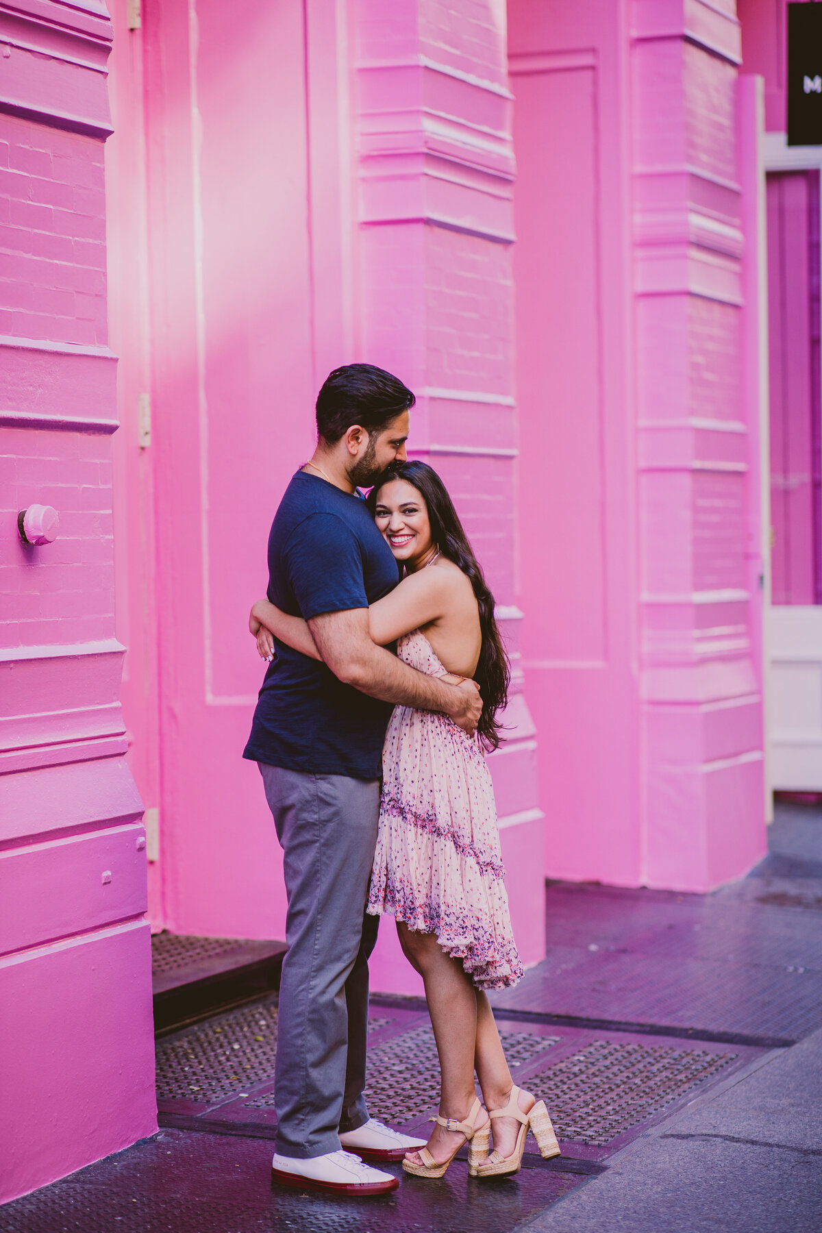 An engaged couple hugging in front of a pink building the marc jacobs store in soho nyc