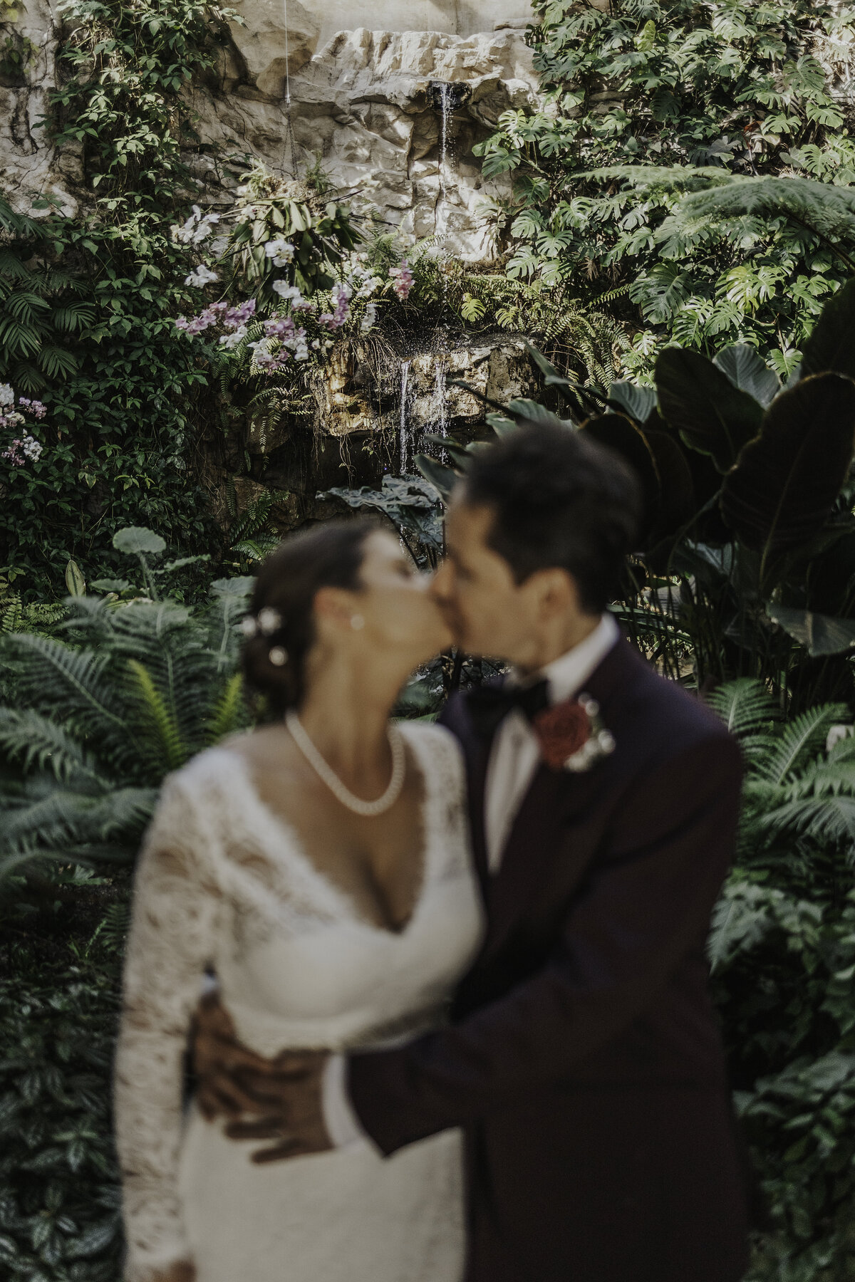 bride and groom kissing in front of a waterfall