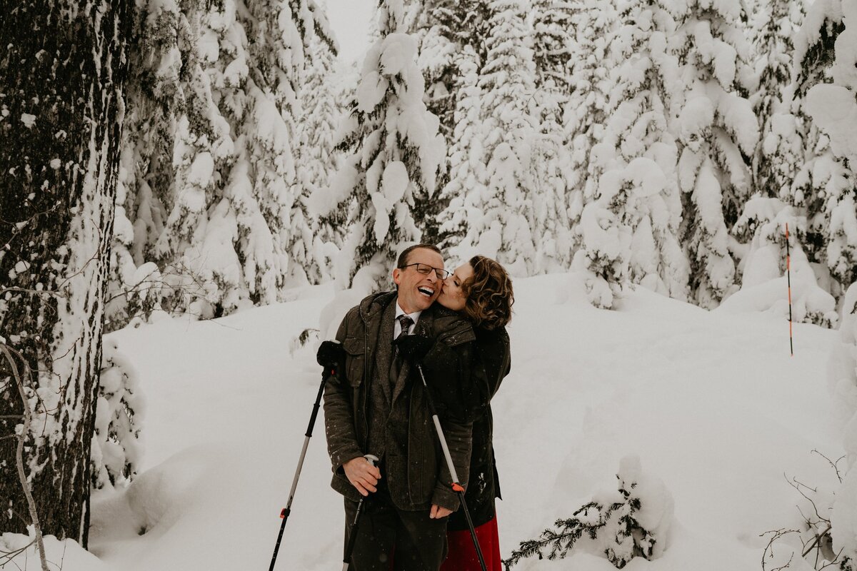 Bride kissing grooms smiling cheek from behind along a snowshoeing trail in Mount Rainier National Park!