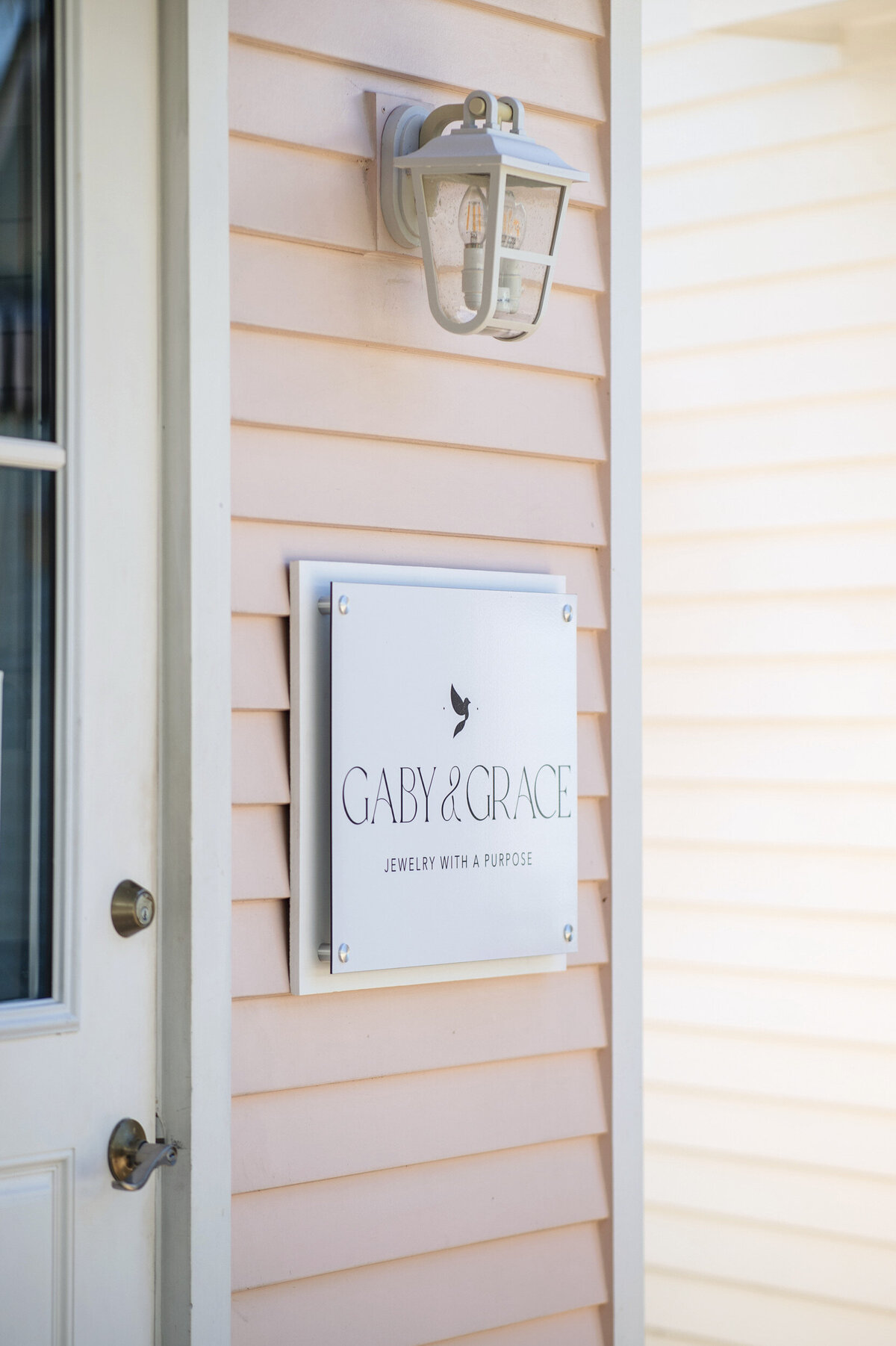 Mounted sign on the exterior of the Gaby & Grace boutique in Galveston, Texas, featuring their logo and tagline “Jewelry with a Purpose” against soft pastel siding.