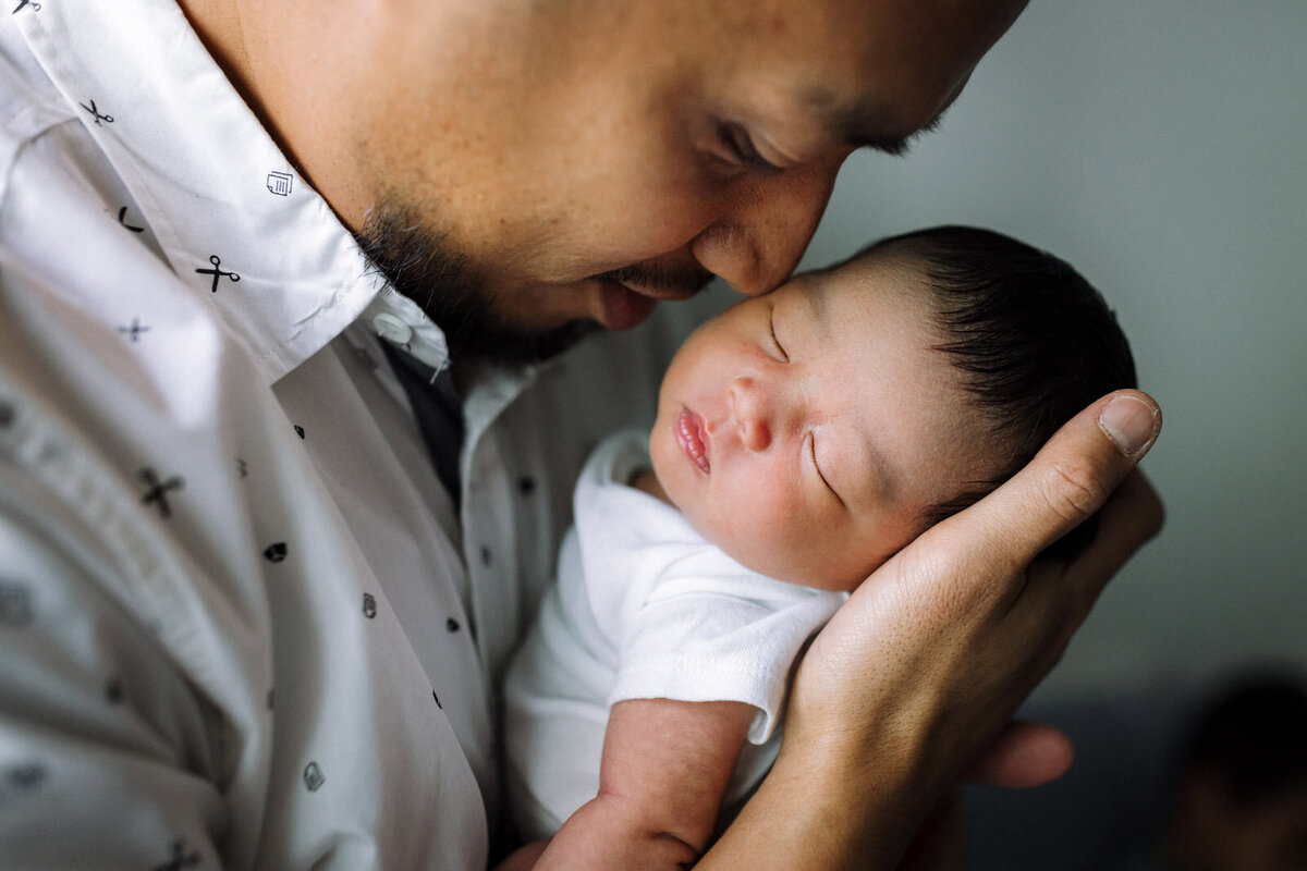 dad holding baby in white onesie close to his face  and resting his nose on side of baby's face