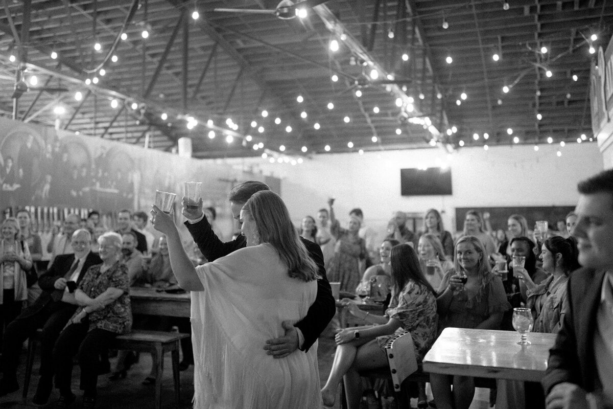 Bride and groom raising a glass in brewery taproom surrounded by guests