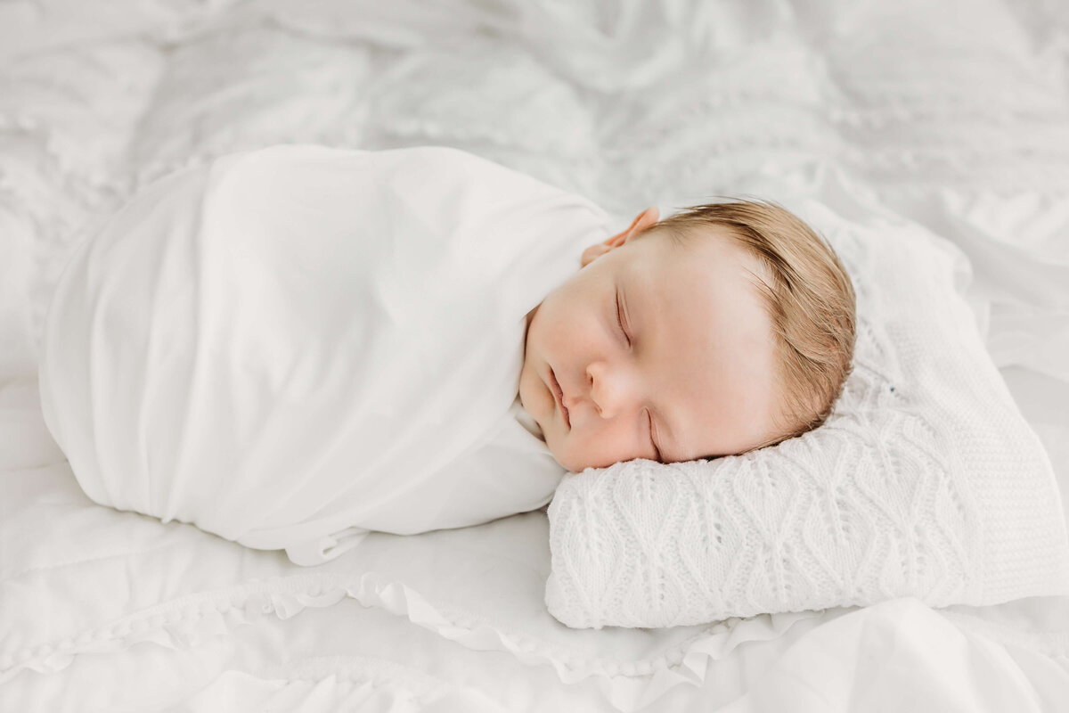 Sleeping wrapped baby in white on bed with blanket
