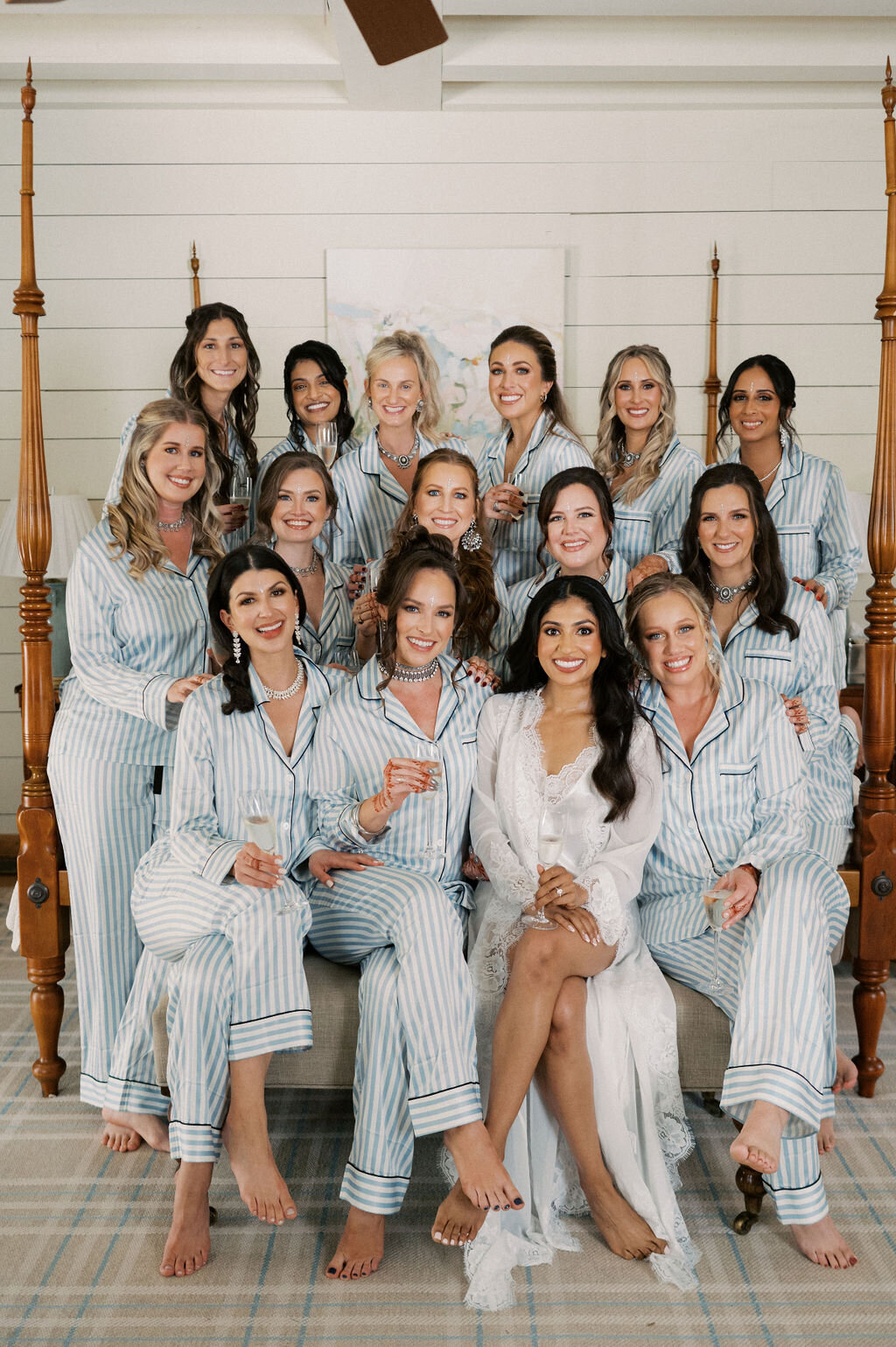 Bride surrounded by bridesmaids in matching striped pajamas holding champagne during getting-ready photos.