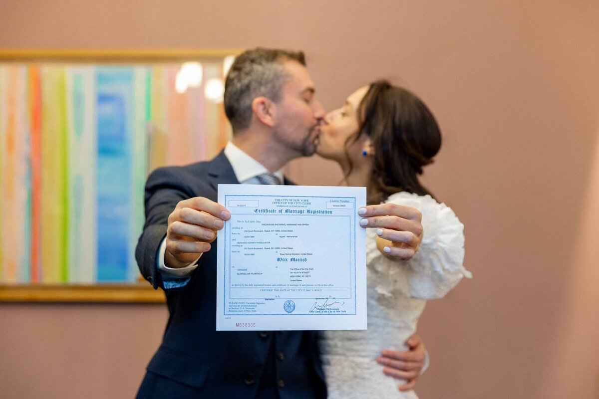 A couple  kissing while holding out their marriage certificate.