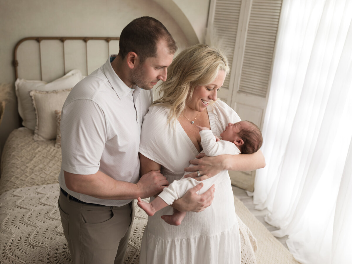 mom and dad holding newborn baby boy in white onesie for studio lifestyle session cleveland newborn photographer