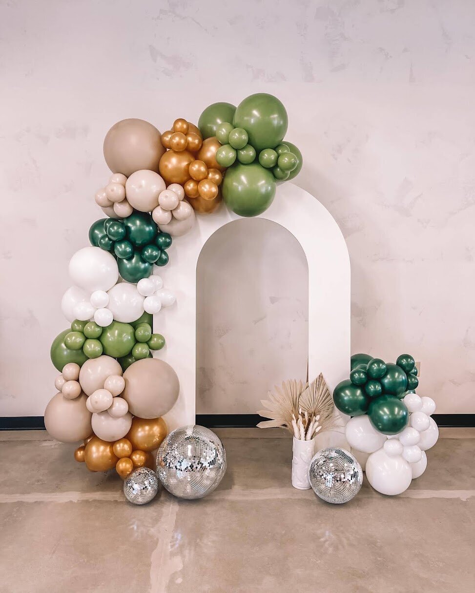 Green, white, and orange balloons on a white rainbow arch with disco balls