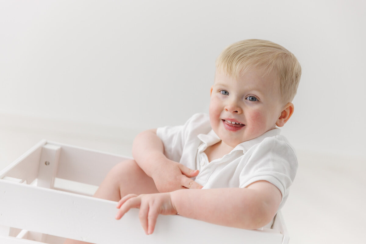 En liten gutt sitter i en hvit eske og smiler mot kamera. Fotografert i Studio Landmark, Fyllingsdalen.
