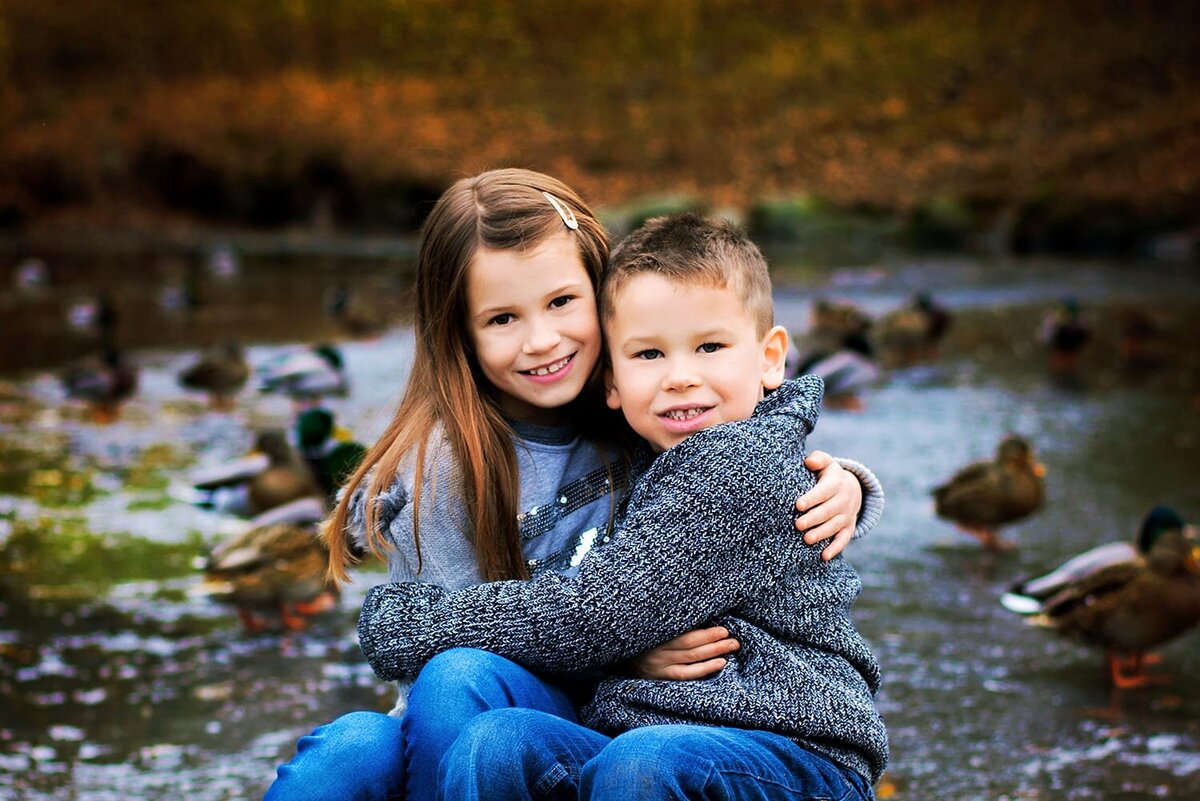 Brother and sister hugging in front of a frozen pond during family photoshoot