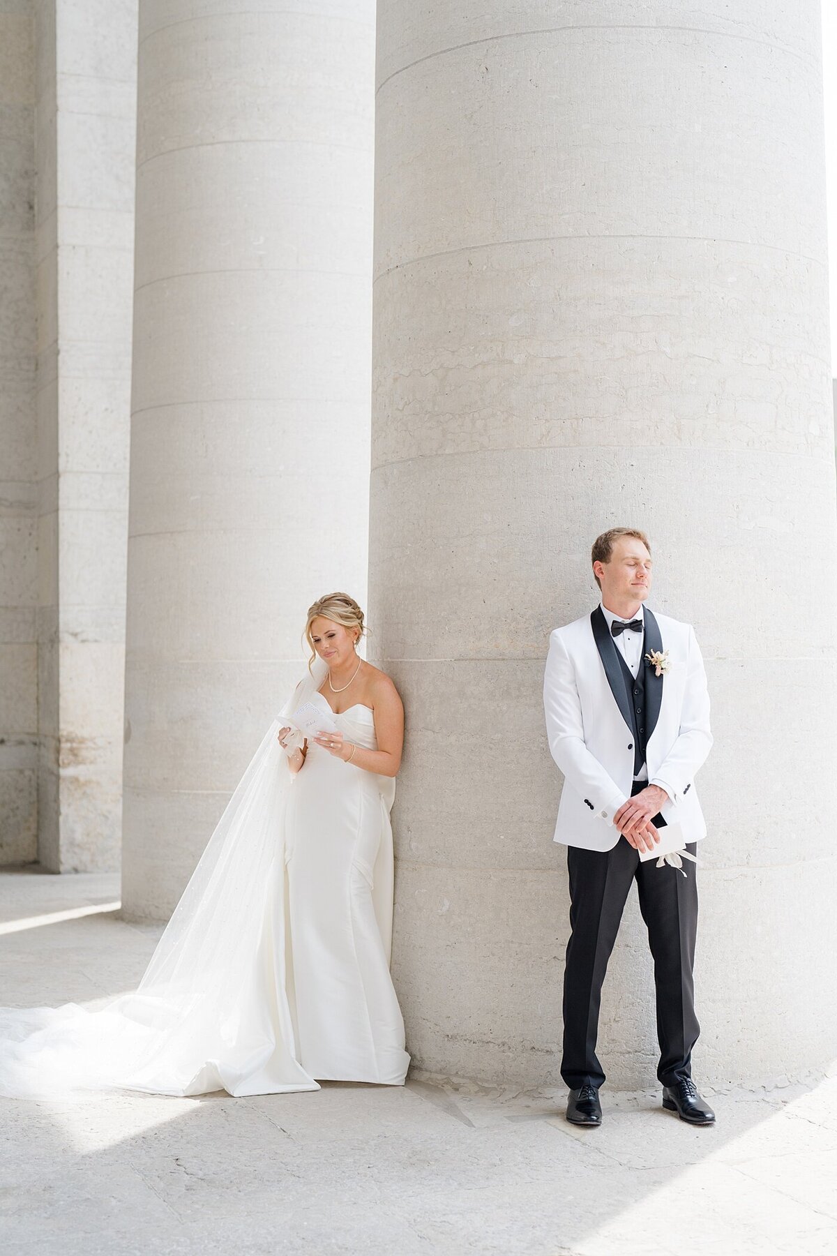 bride and groom standing on opposite side of a pillar while reading private vows to each other