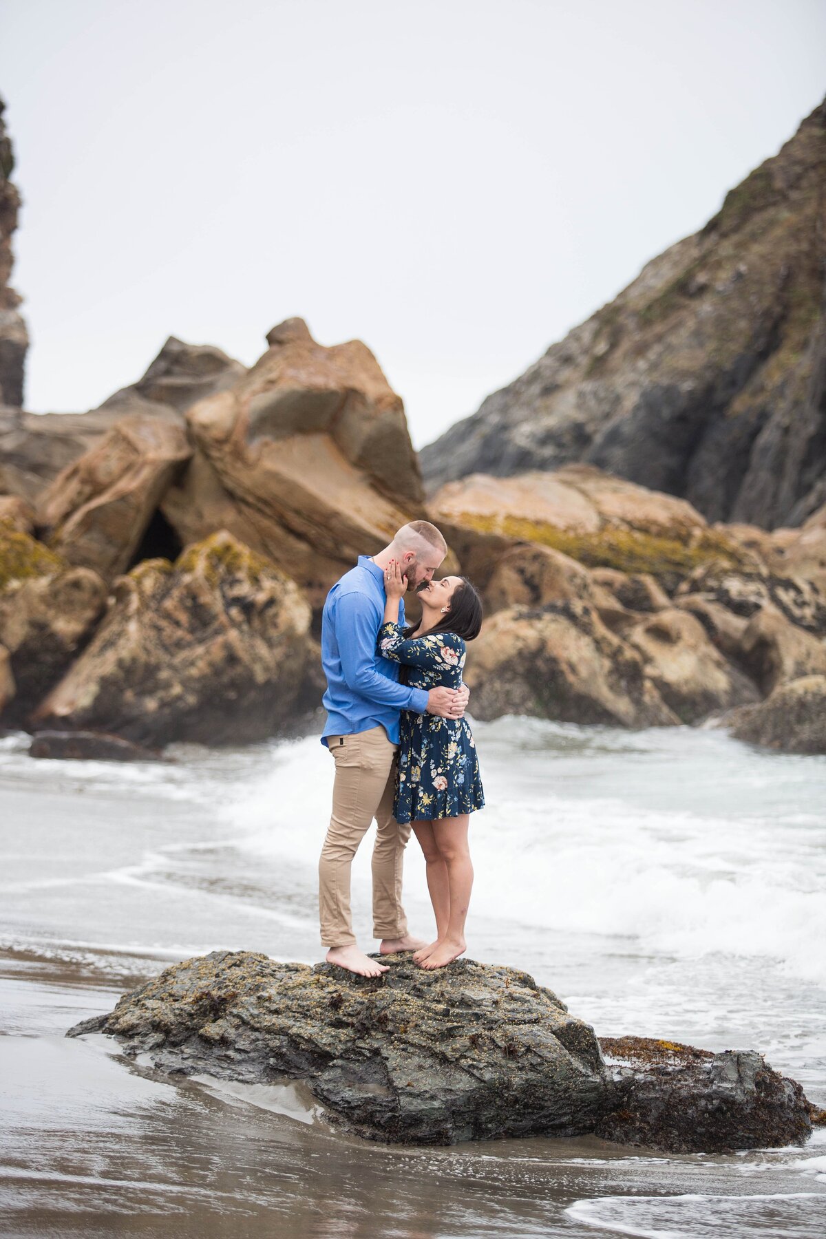 couple kissing and standing on rock in the ocean