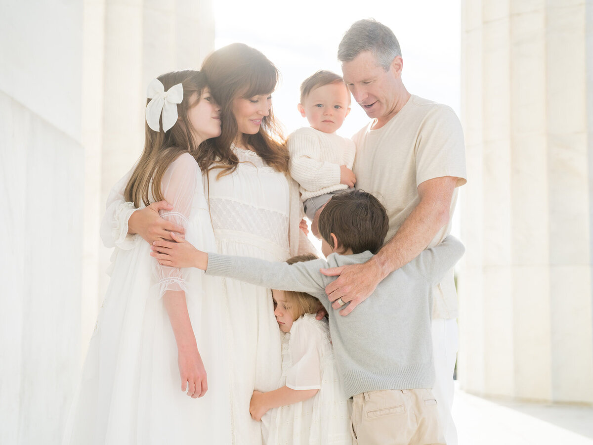 Mother and father hug their four children while standing in the Lincoln Memorial.