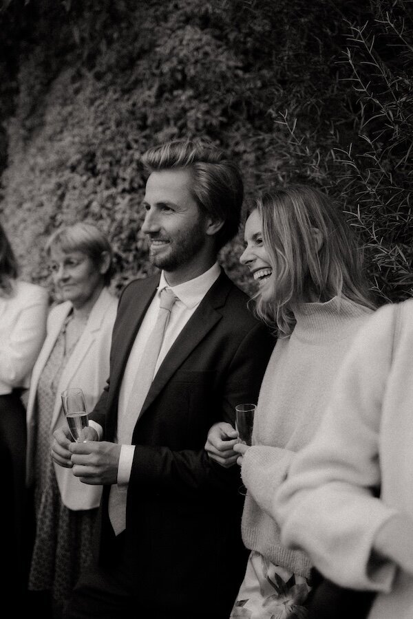Un couple d'invités trinque avec éclats de rire. Photographie de mariage en noir et blanc par Kamescop.