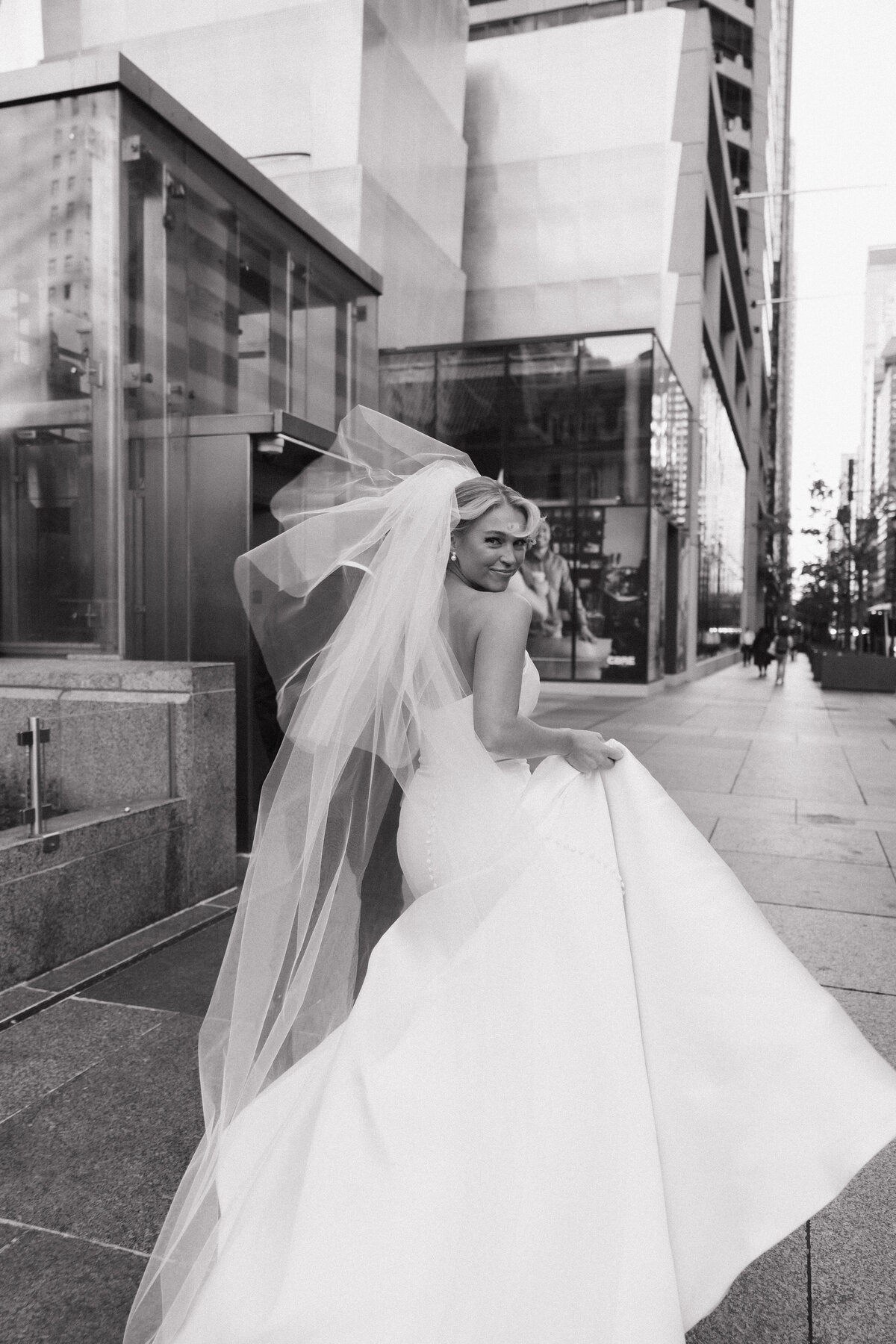 Bride and groom walking on the sidewalk in Philadelphia, Pennsylvania with the wind blowing through her veil. 