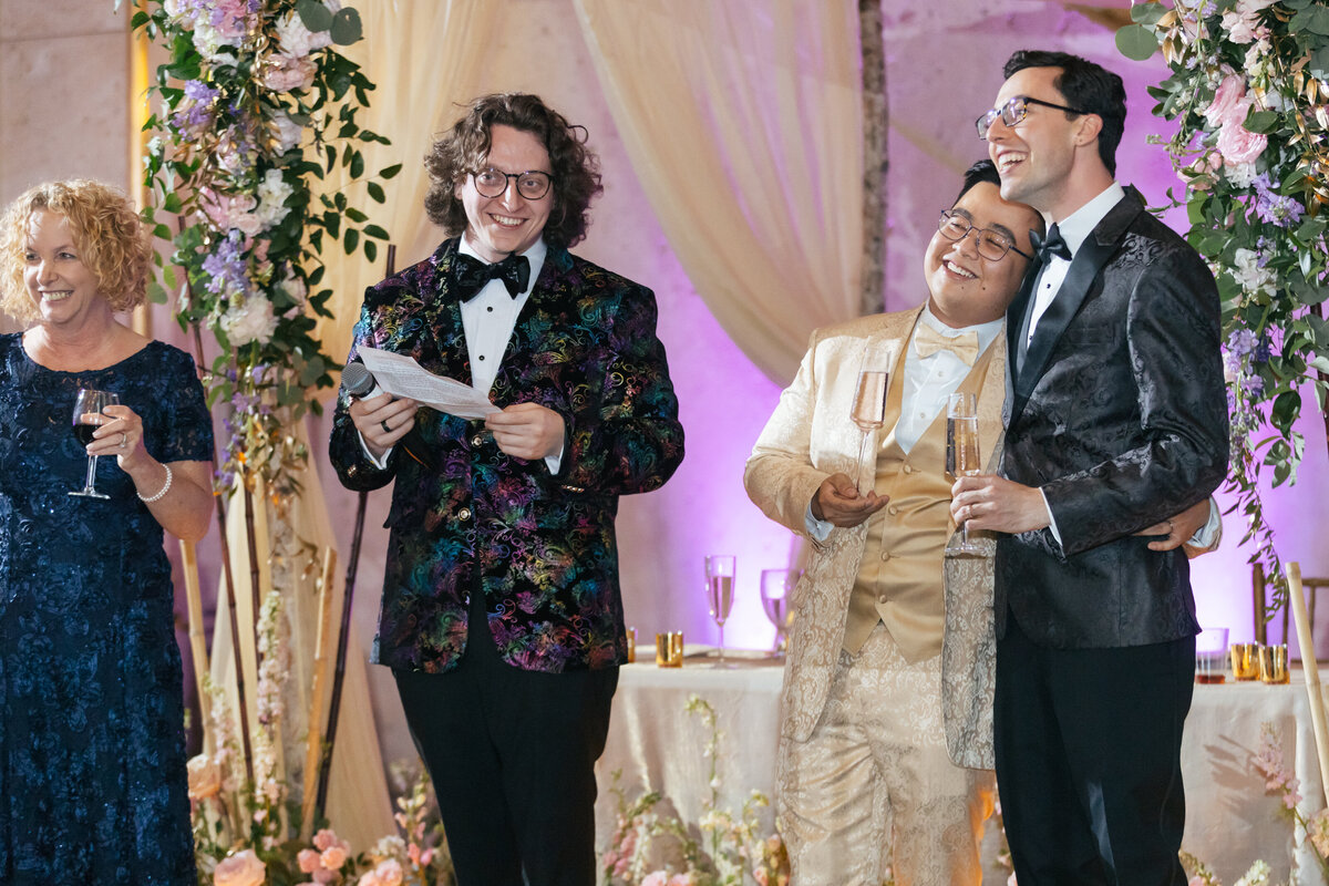Candid photo of two grooms at their wedding reception during toasts at The Hall of State