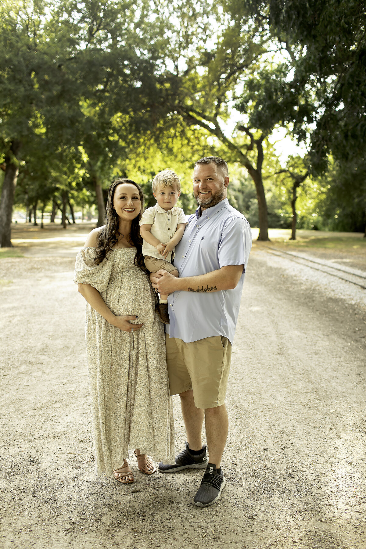A beautiful maternity photo at Trinity Park, with mom, dad, and big brother looking at the camera, all smiling together as they enjoy a joyful moment as a family, captured by Chunky Monkey Photography.