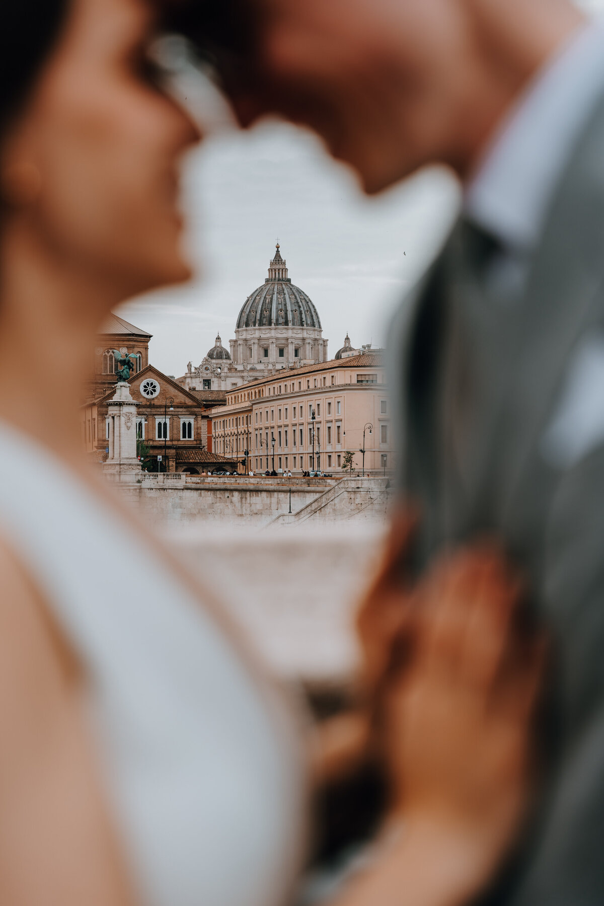 Close-up of couple leaning in with St. Peter’s Basilica blurred in background.