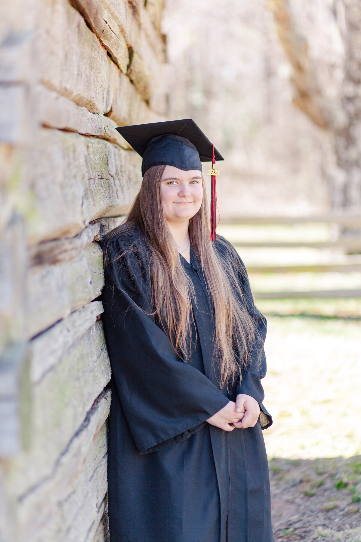 Senior girl in cap and gown leaning on a barn