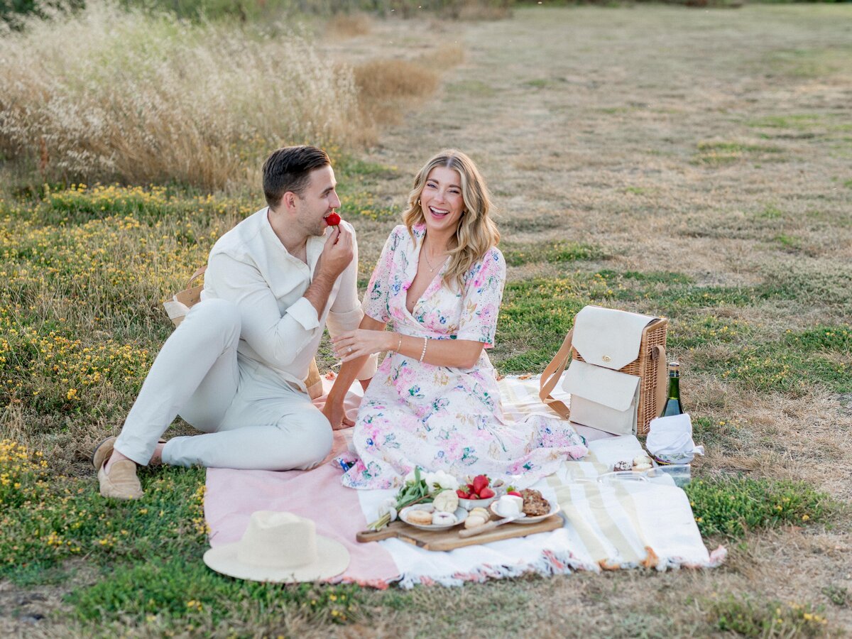 Whimsical engagement picnic in the golden fields—laughing, sharing strawberries, and soaking up the romance.